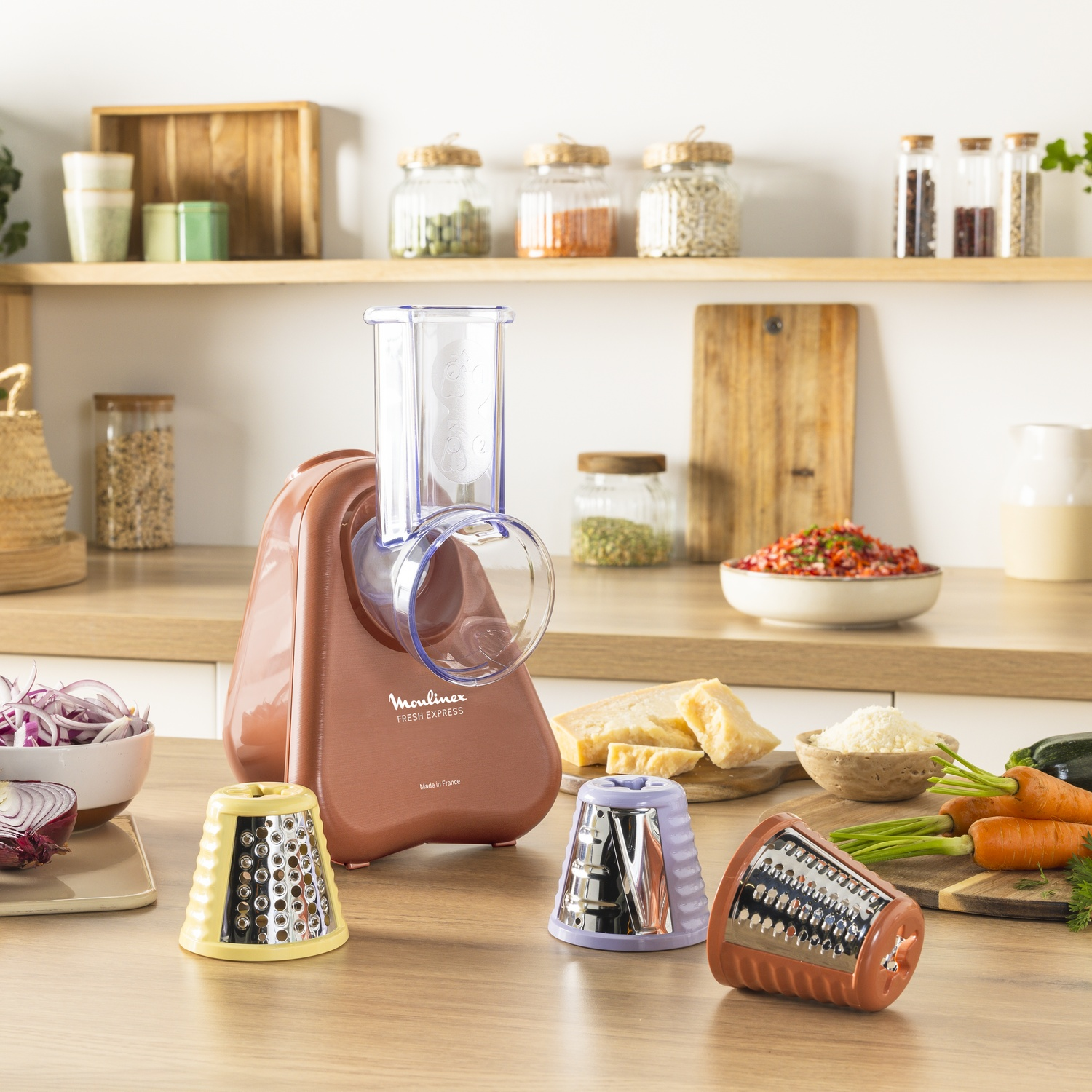 A Moulinex Fresh Express, with three attachments, sits on a wooden counter with vegetables and spices in the background.