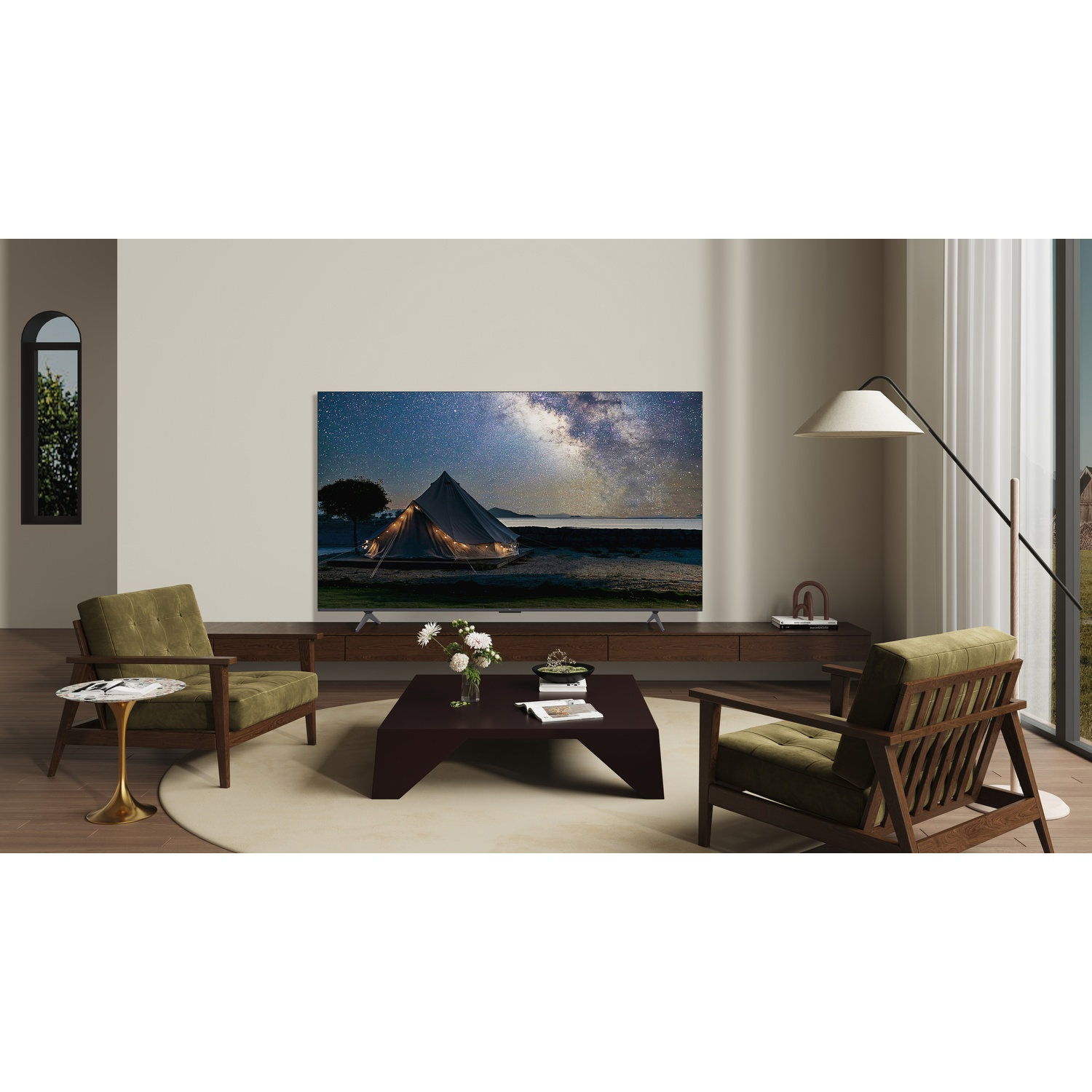 Soggiorno con TV che mostra un cielo stellato. Sono presenti anche sedie verde oliva, tavolo marrone, fiori bianchi, lampada e finestra.