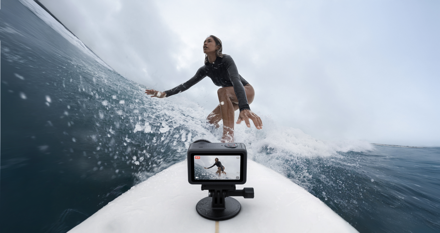 Un surfista monta una ola. Una cámara en una tabla de surf captura la acción. El cielo está nublado.