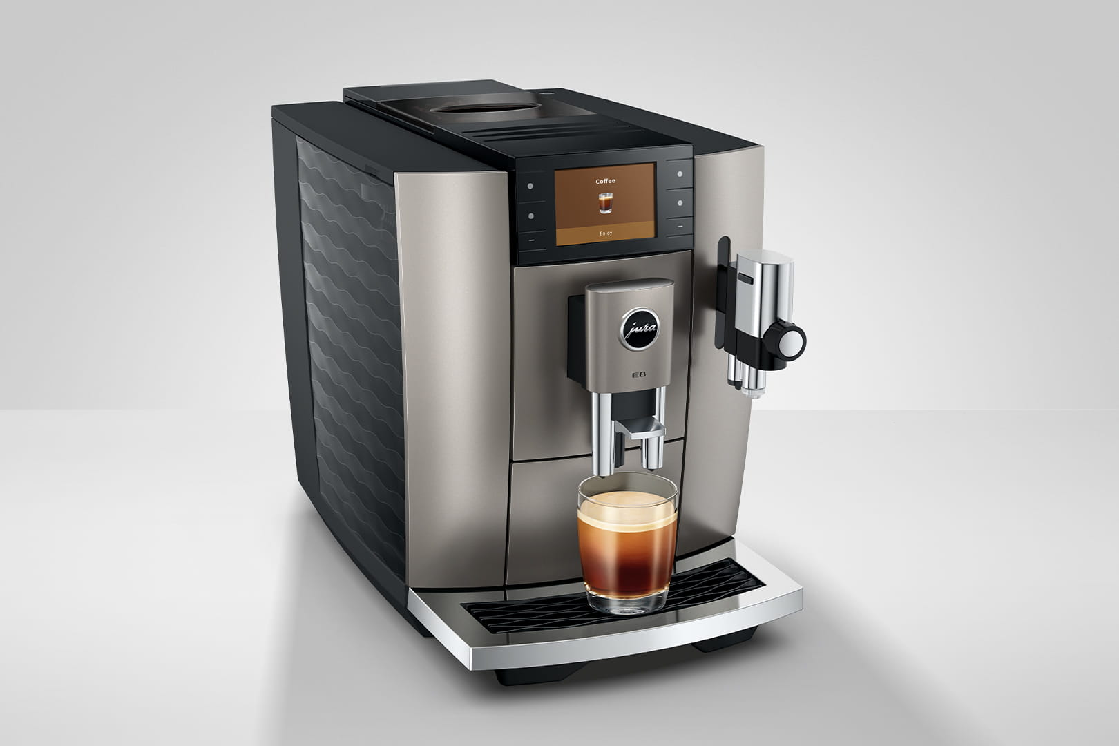 Una macchina da caffè Jura E8 argento e nera. Un bicchiere di espresso è davanti. Lo schermo mostra una tazza di caffè.