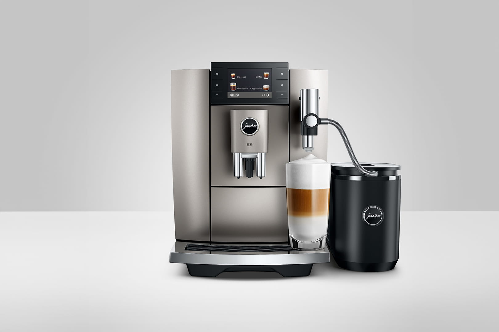 Una macchina da caffè Jura E8 con un latte macchiato. La macchina è argento, un contenitore del latte nero è a destra.