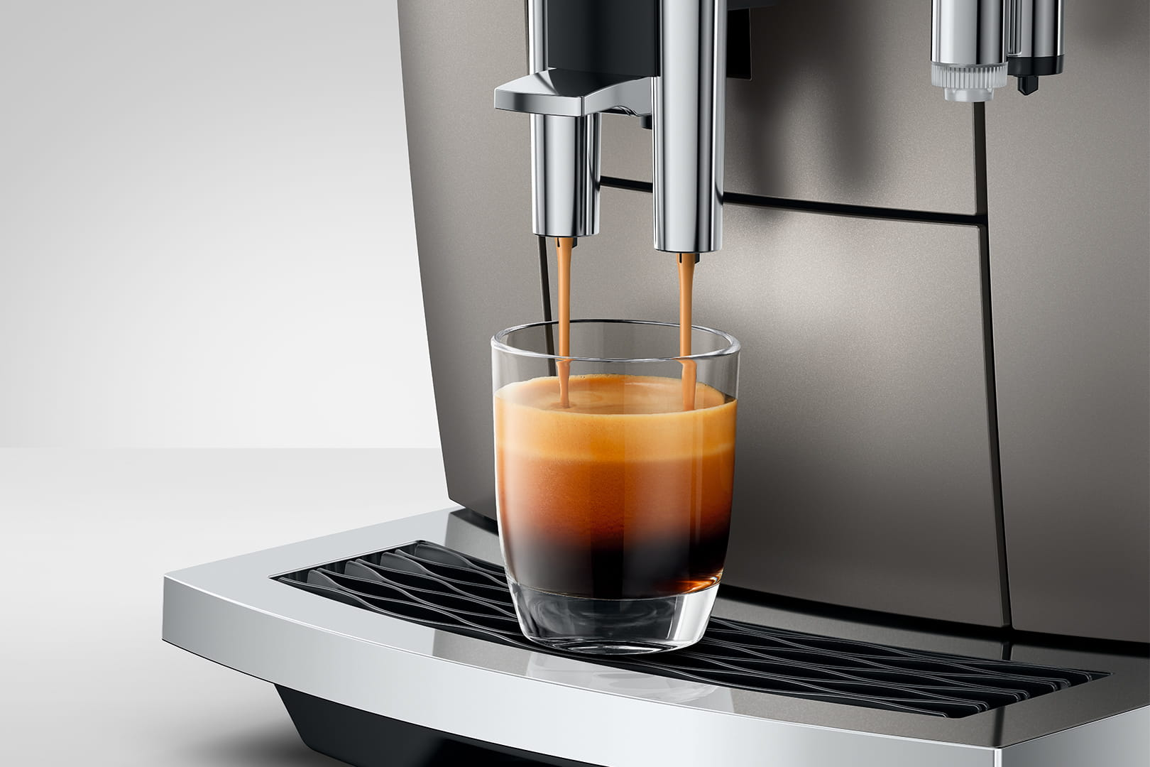 Macchina per espresso che eroga caffè in un bicchiere. Il caffè è marrone scuro con una crema densa. Macchina cromata e vetro.