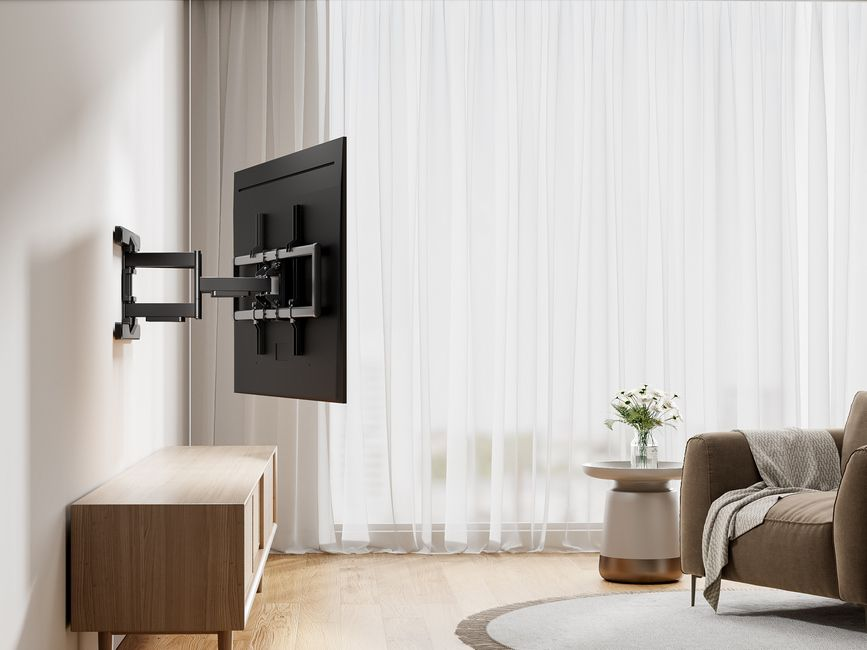 Salon avec une télévision fixée au mur. Un meuble en bois et un canapé avec une couverture sont visibles.