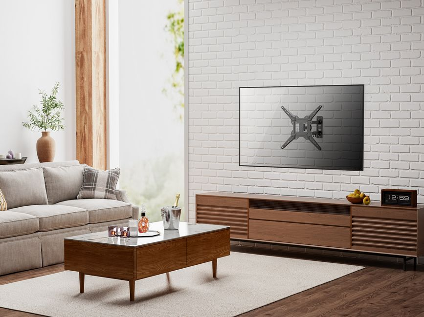 Salon avec canapé, table basse et télévision sur un mur de briques blanches. Une horloge et des fruits sur un meuble en bois.