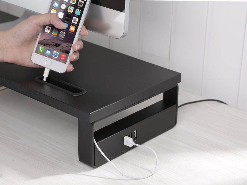 Une main tient un téléphone blanc avec un câble de chargement connecté. Le téléphone repose sur un bureau noir.