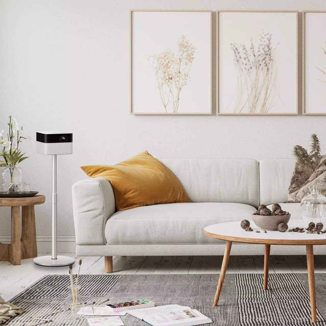 Soggiorno con divano bianco, cuscino giallo, proiettore e stampe botaniche incorniciate sul muro.