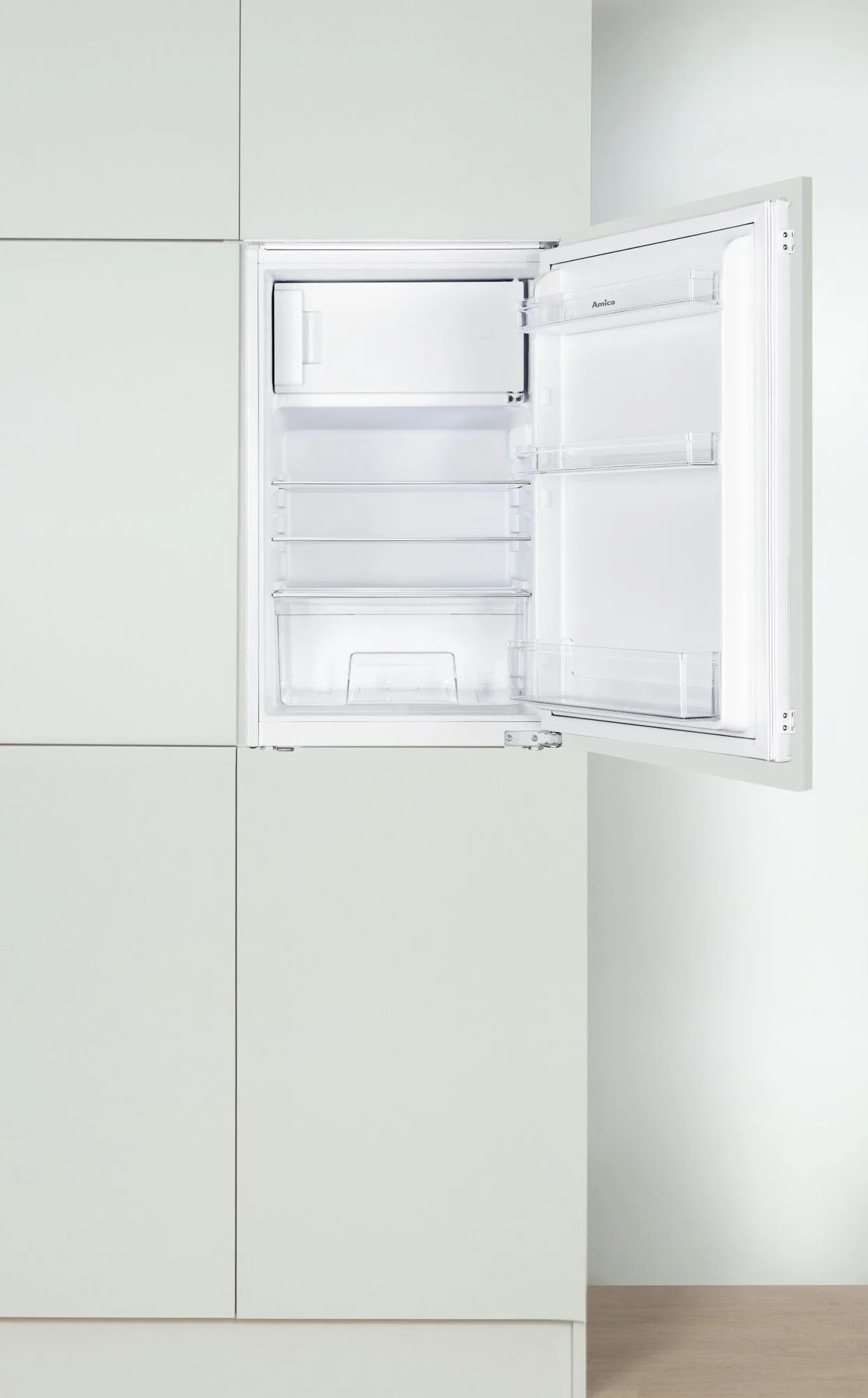 Otwarta biała lodówka wbudowana w jasnoszare szafki. W środku znajdują się półki i zamrażarka. Widoczna jest nazwa marki 'Amica'.