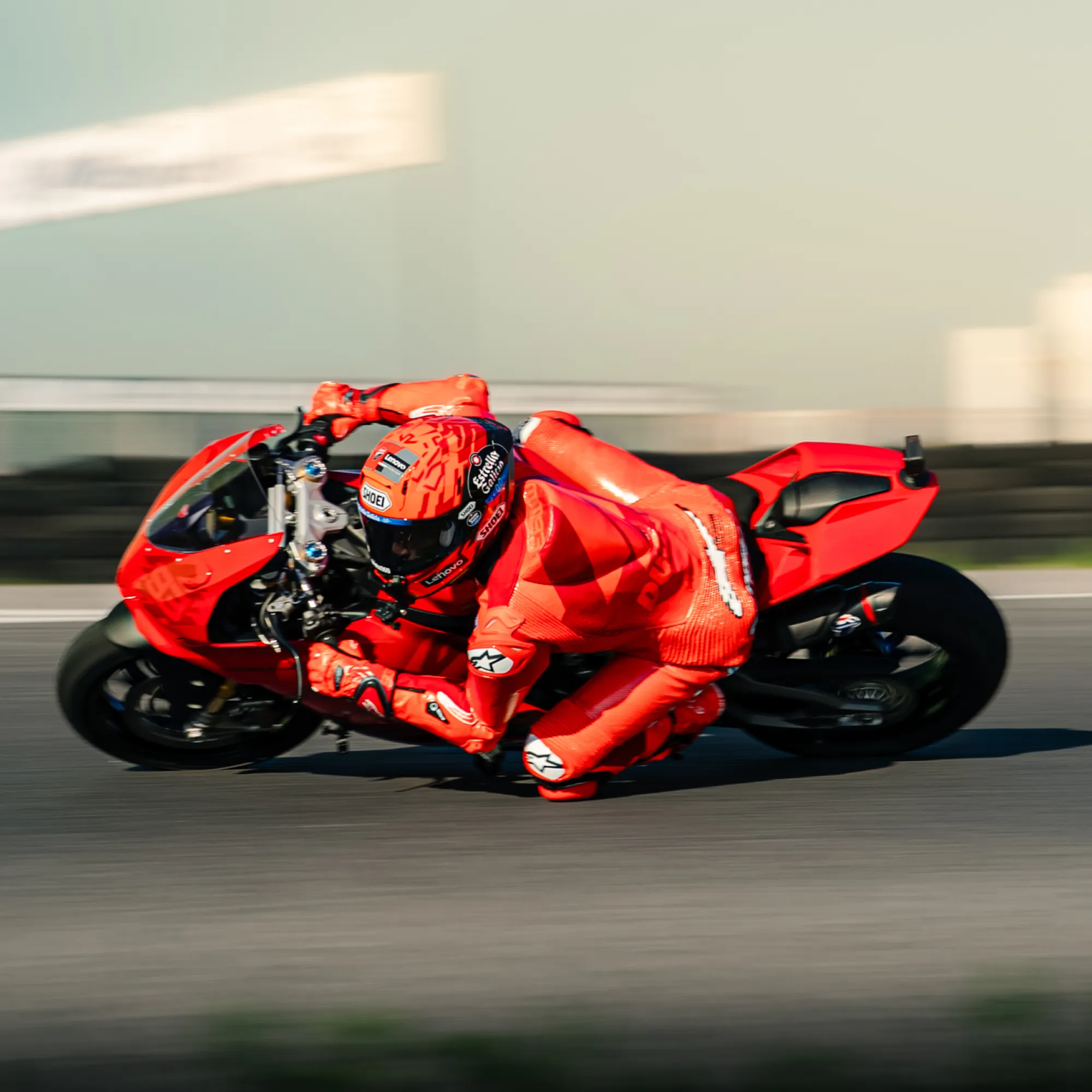 Ein rotes Motorrad rast auf einer Rennstrecke. Der Fahrer trägt einen roten Anzug und Helm, tief geneigt. Verschwommener Hintergrund.