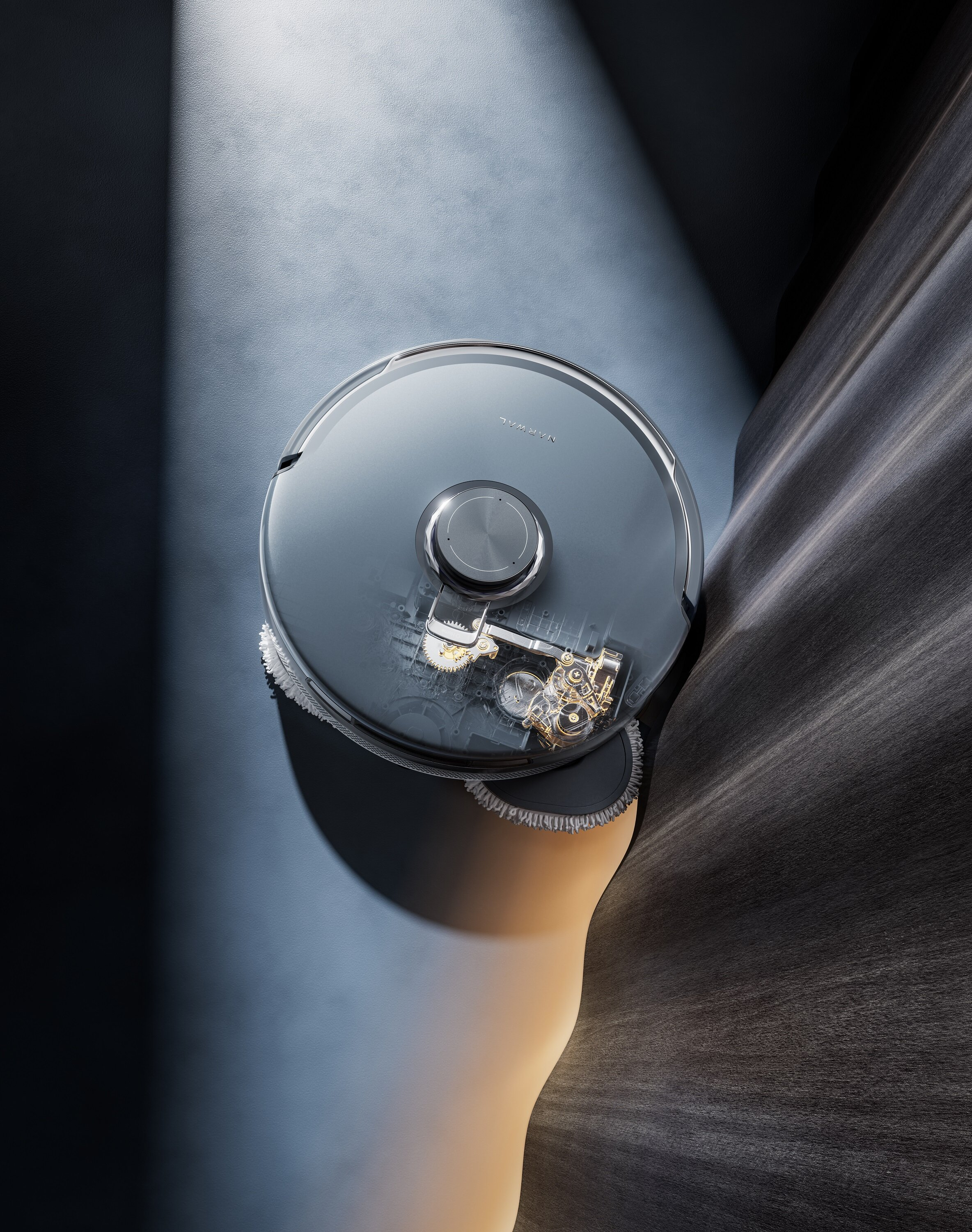 Robot odkurzający z przezroczystą pokrywą. Znajduje się na ciemnoniebieskiej i szarej powierzchni.