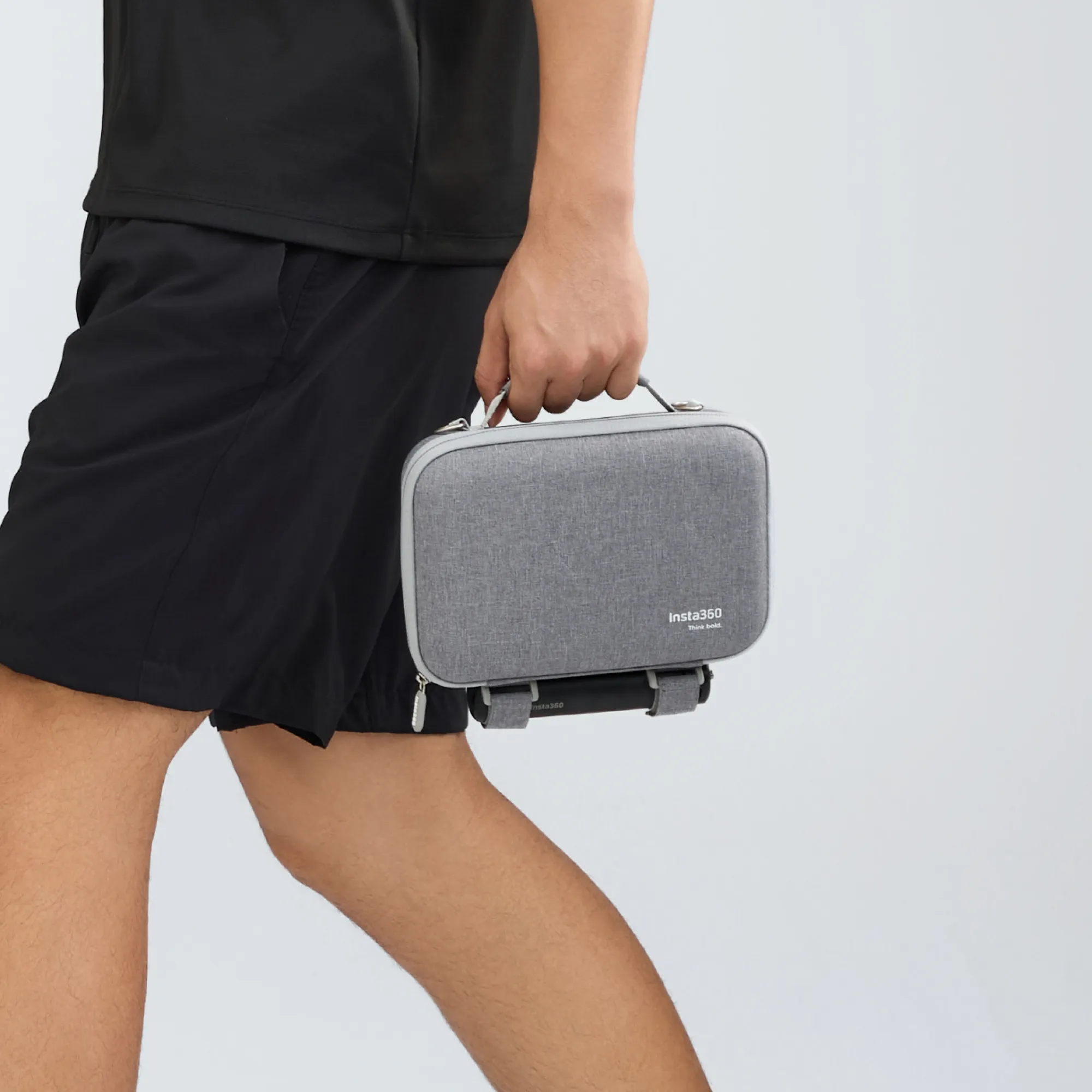 Eine Person hält eine graue Insta360-Tasche. Sie trägt eine schwarze Shorts und ein schwarzes Hemd. Der Hintergrund ist weiß.