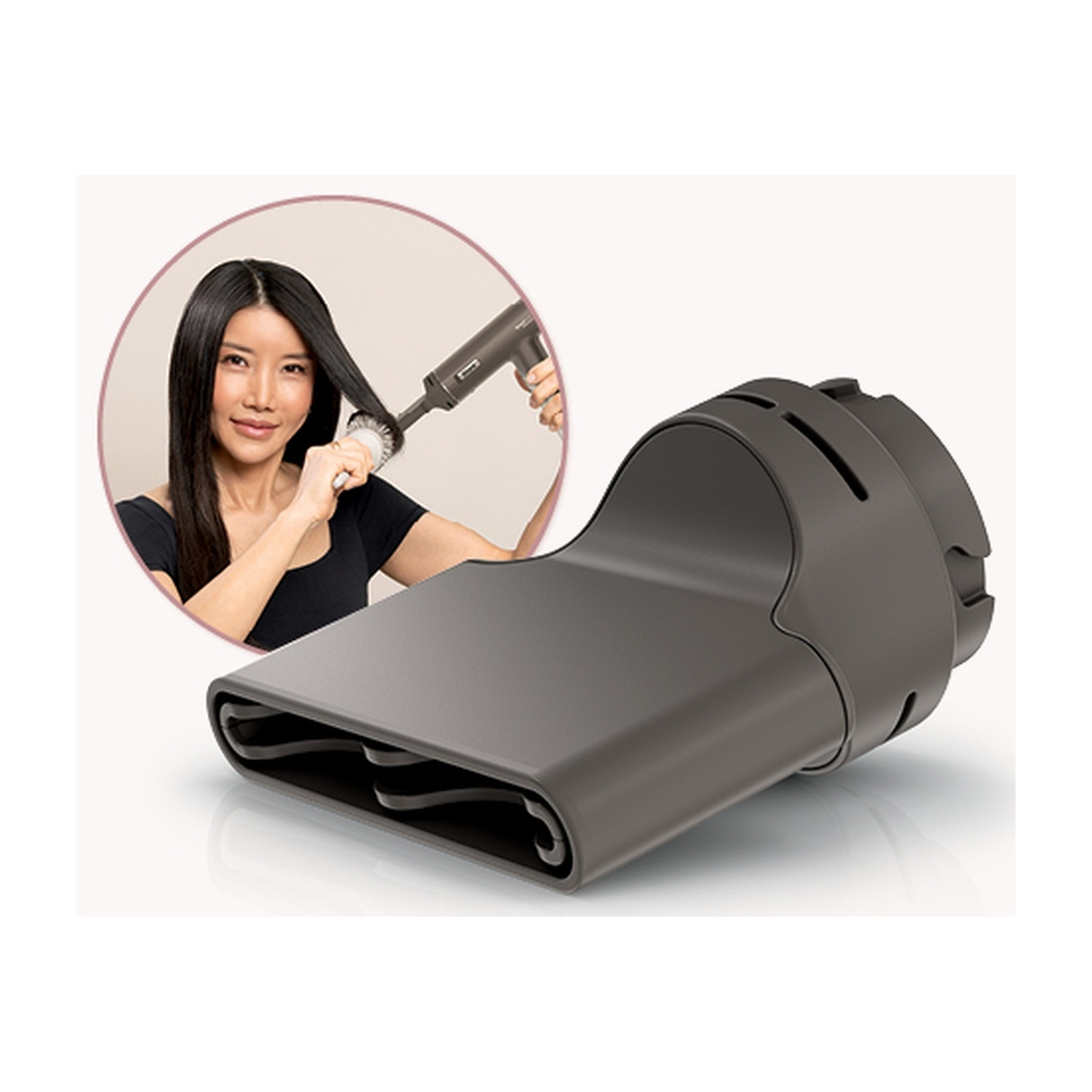 Una donna si spazzola i capelli con un asciugacapelli. Un accessorio dell'asciugacapelli è in primo piano. È grigio, curvo ed elegante.