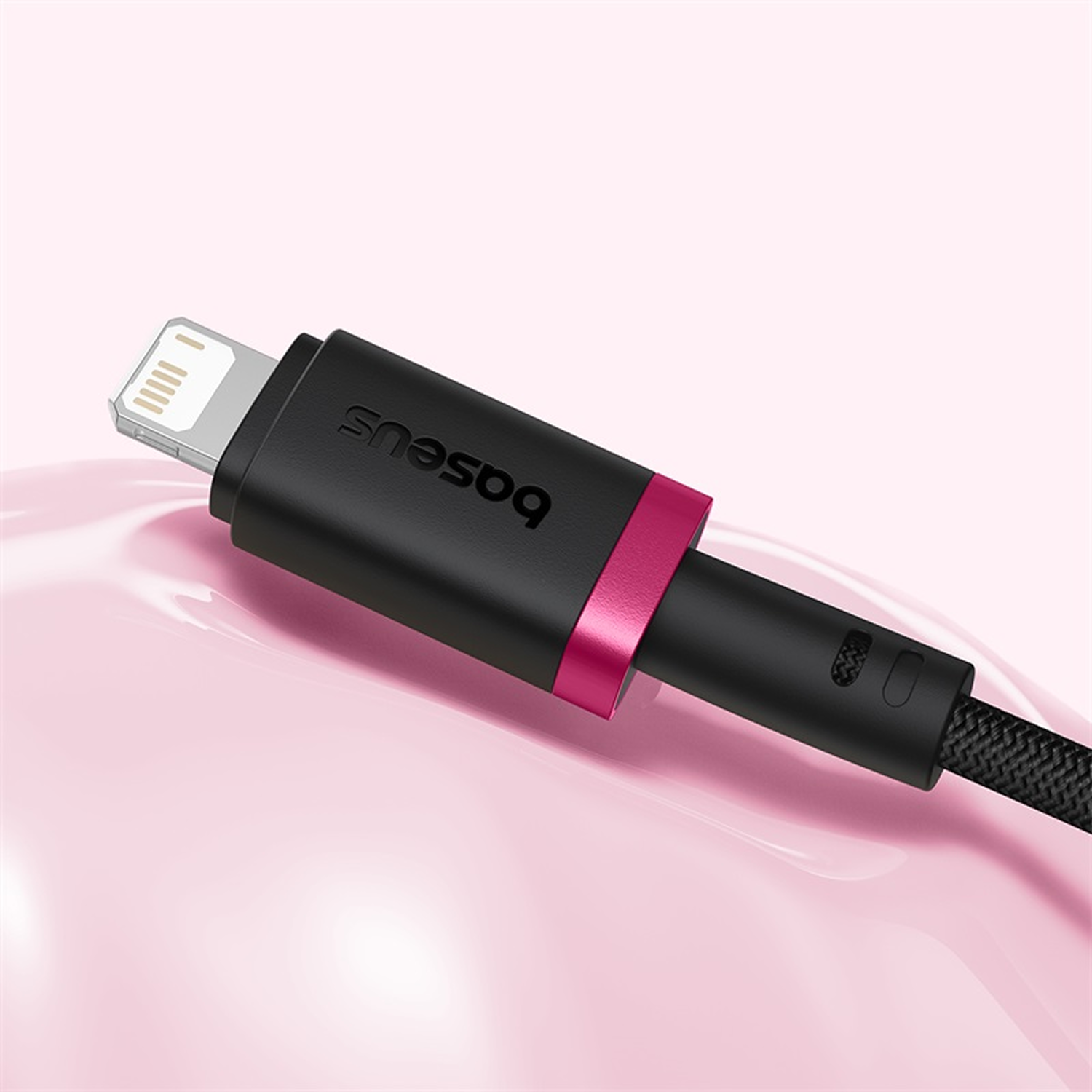 Un cable de carga Baseus negro con un acento rosa y un conector Apple Lightning, sobre una superficie rosa brillante.