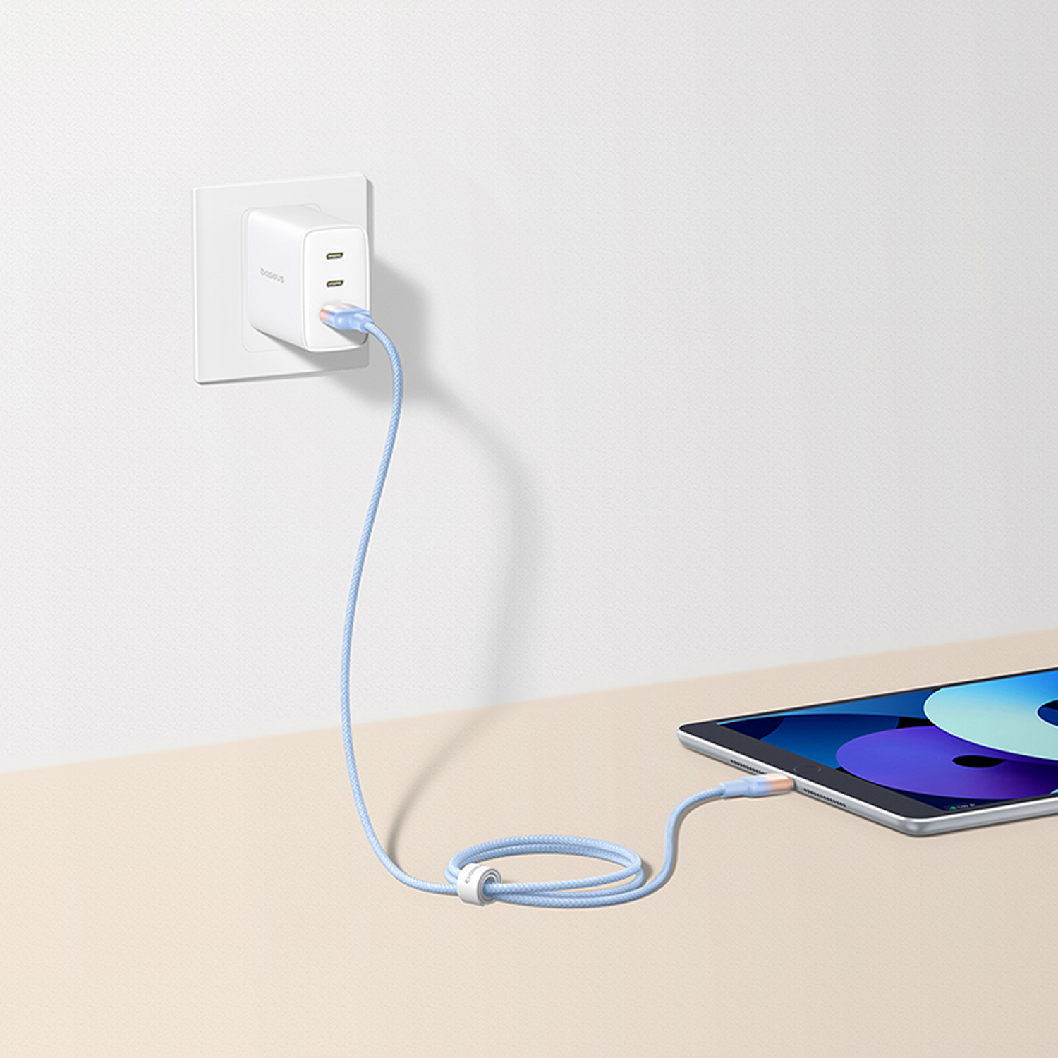 Un adaptador de corriente blanco enchufado a la pared, con un cable azul conectado a una tableta sobre una superficie beige.