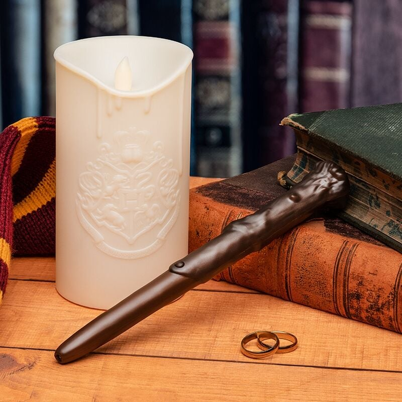 Una vela crema con el escudo de Hogwarts, una varita, dos anillos y libros sobre una superficie de madera.