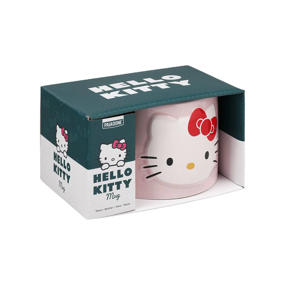 Taza de Hello Kitty en una caja. La taza es rosa con un lazo rojo y la cara de Hello Kitty. La caja es verde y blanca.