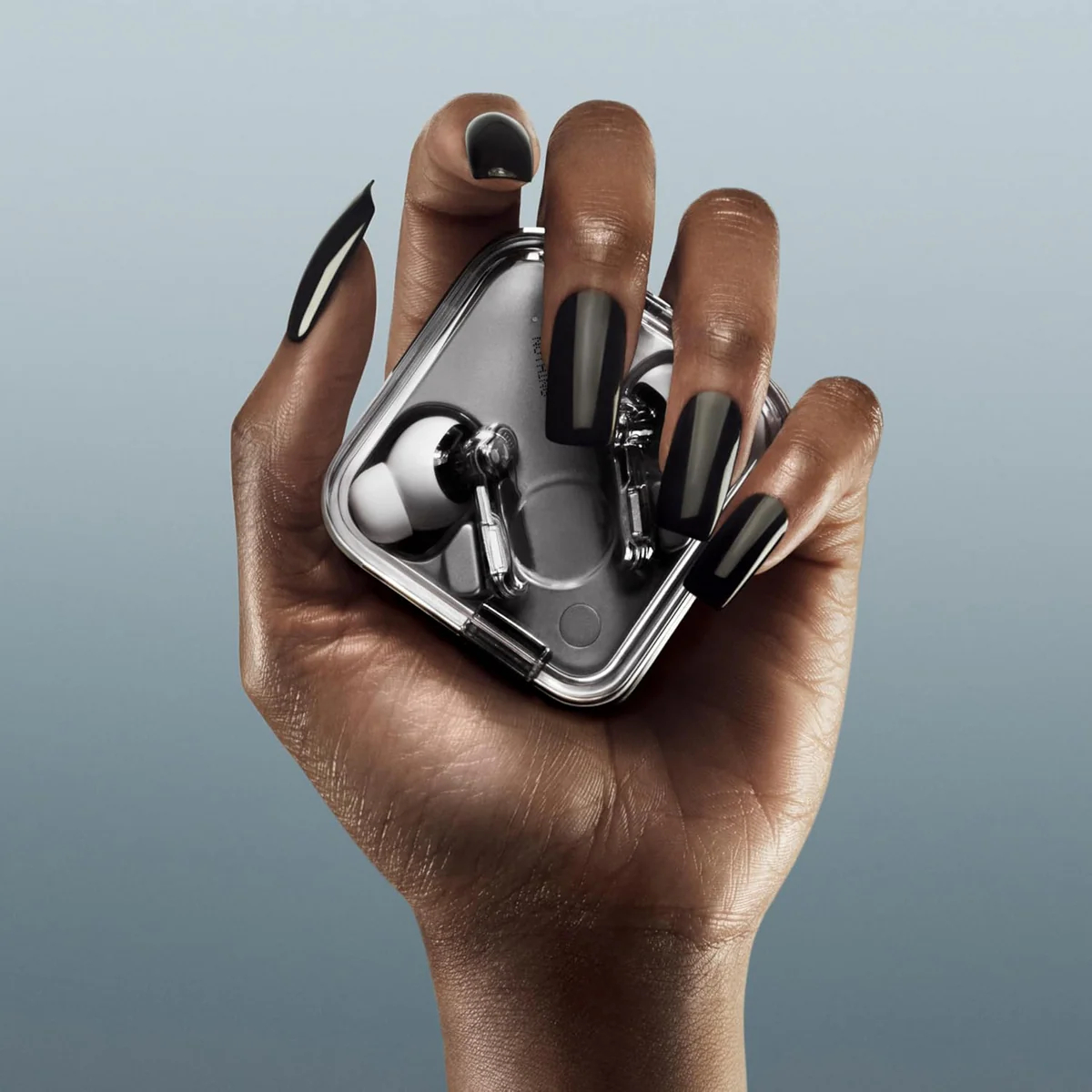 Una mano con esmalte de uñas negro sostiene una funda transparente con auriculares blancos. El fondo es azul degradado.