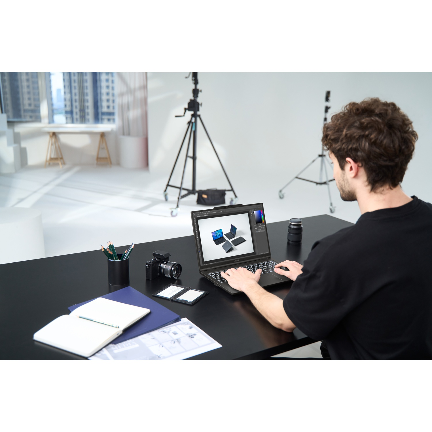 Een persoon gebruikt een laptop op een zwarte tafel. Camera, notitieboek en potloden op de tafel. Studio-achtergrond.