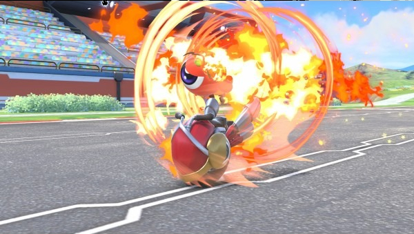 Un personnage rouge sur un véhicule est entouré de feu sur une piste de course. Le fond montre un stade et des collines vertes.