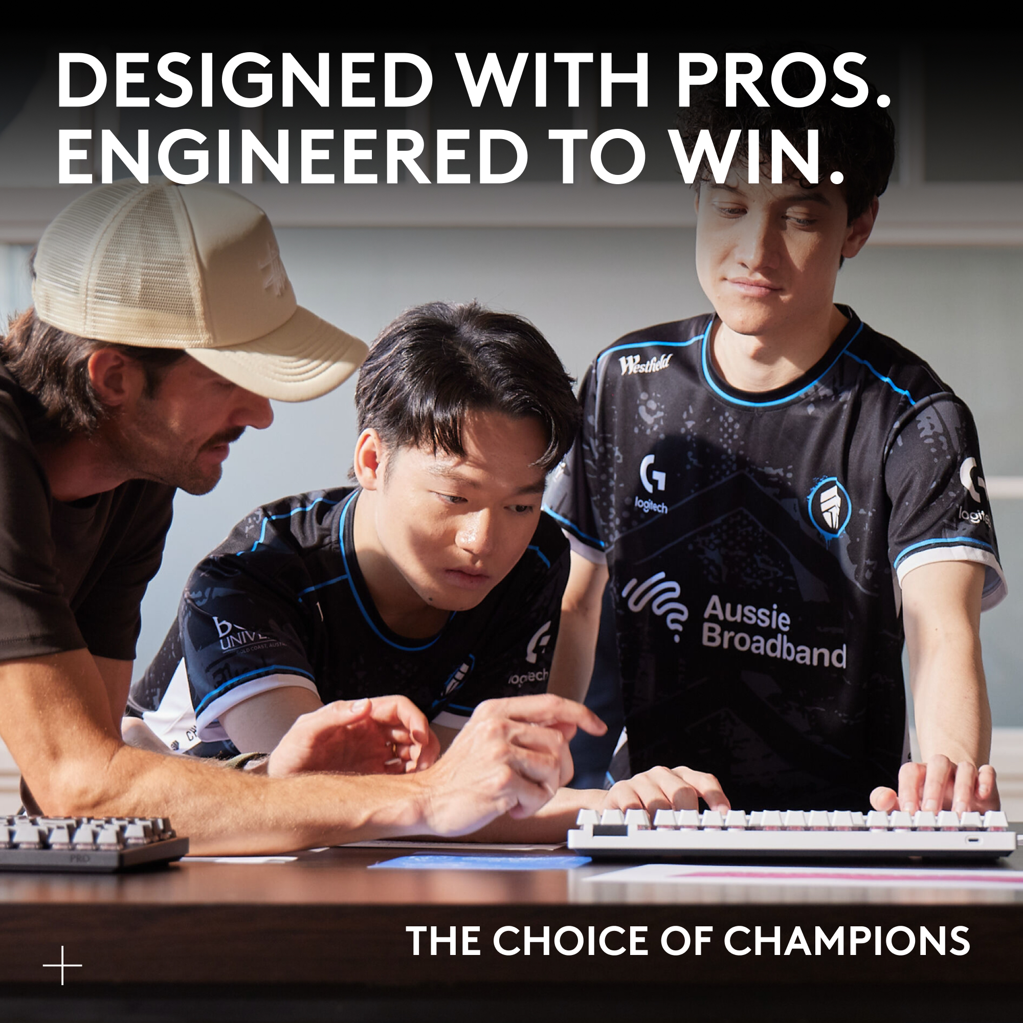 Drei E-Sportler untersuchen eine Tastatur. Einer trägt einen Hut. Text: Entworfen mit Profis. Entwickelt, um zu gewinnen.