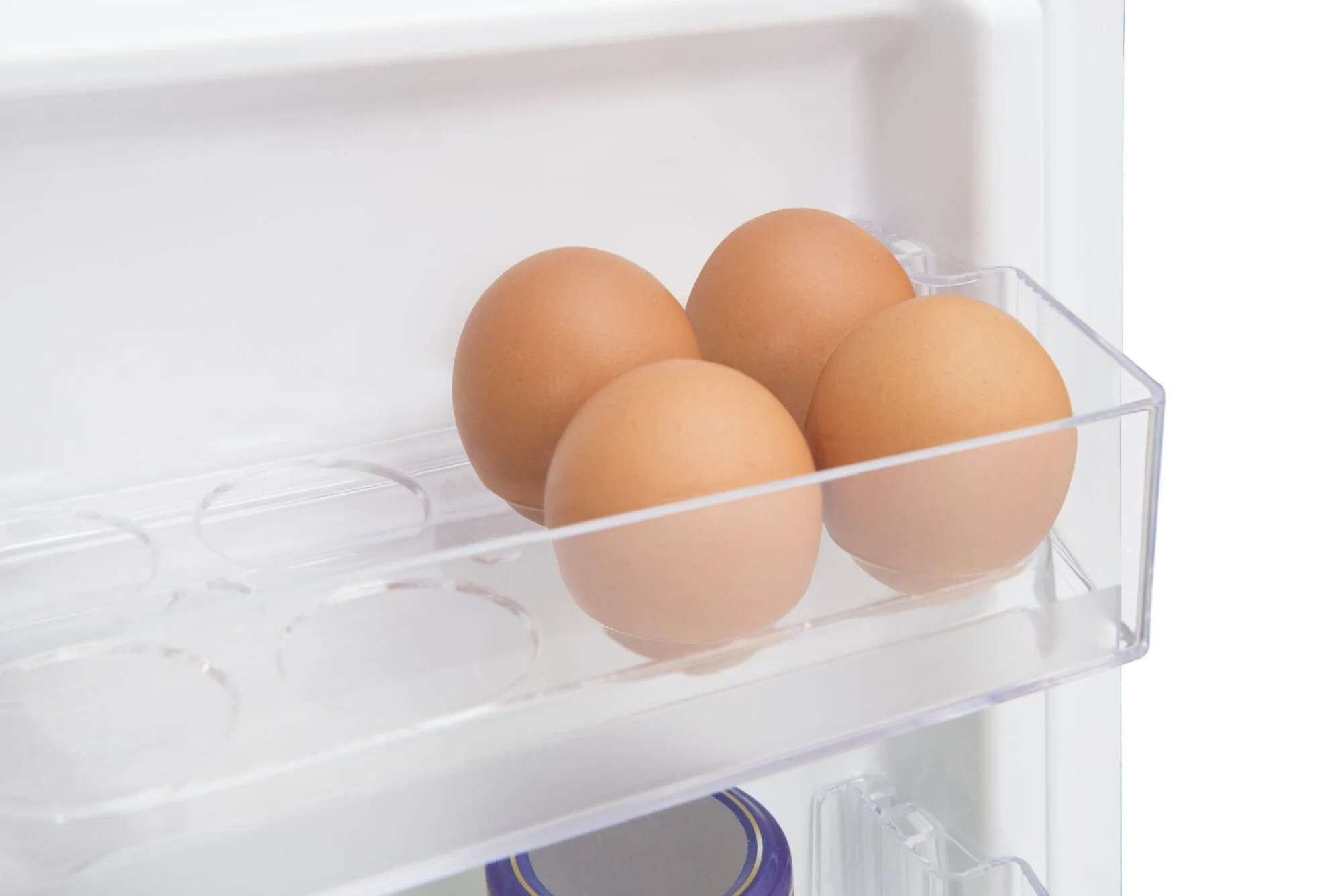 Cztery brązowe jajka w przezroczystym plastikowym pojemniku w białej lodówce. Jajka są w centrum uwagi.