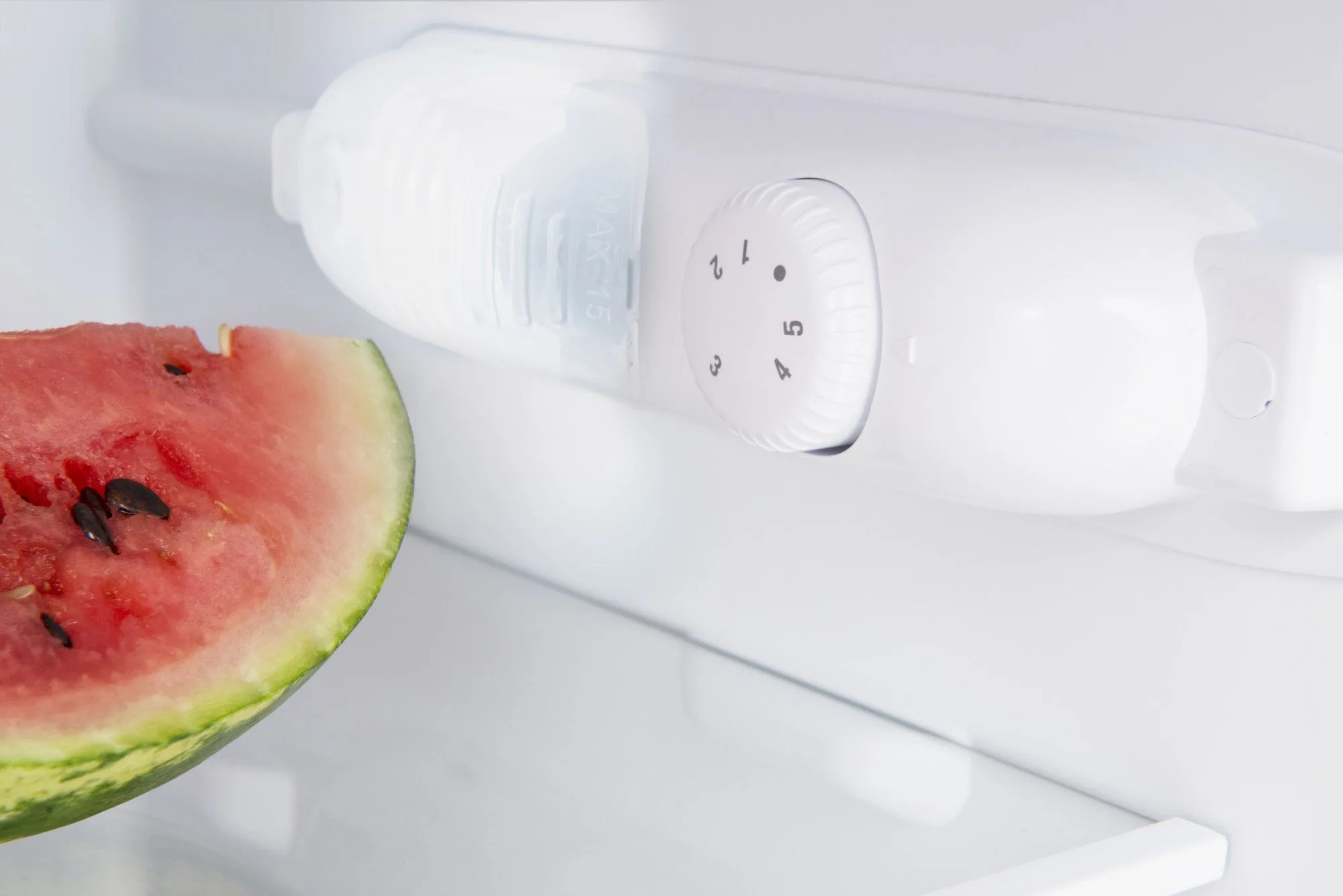 W lodówce plasterek arbuza z czarnymi pestkami znajduje się w pobliżu białego panelu sterowania. Na tarczy są liczby.