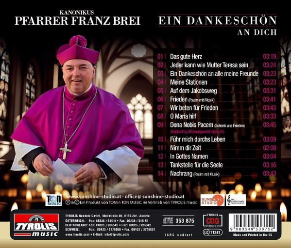 Ein Mann in lila Robe und Hut hält Papiere, eine Kreuzkette, der Hintergrund ist eine Kirche mit Kerzen.