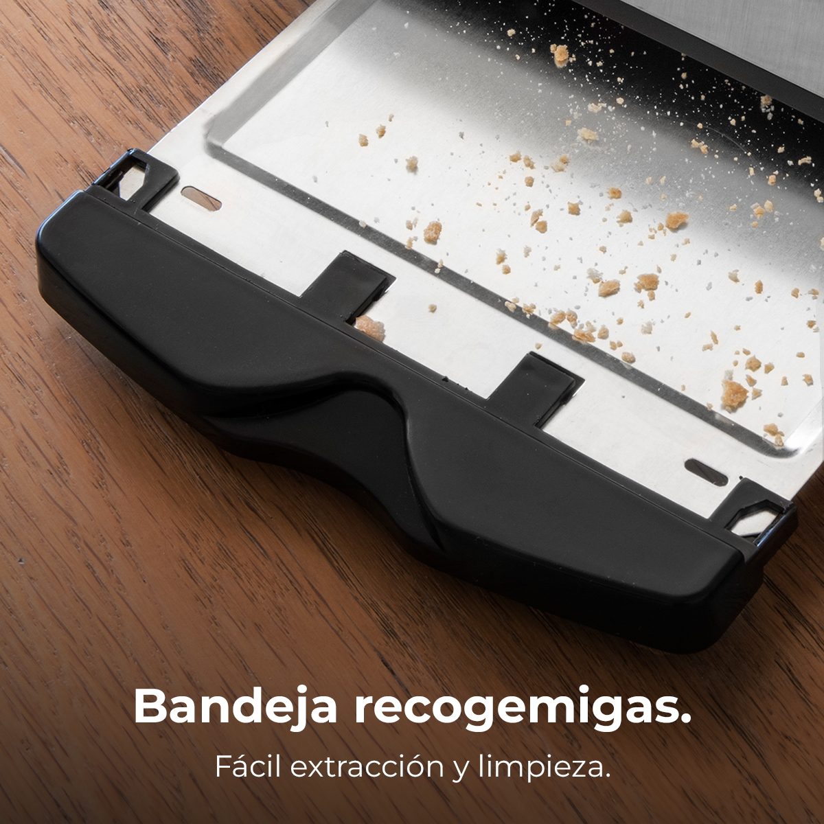 Primer plano de la bandeja recogemigas de una tostadora. La bandeja es negra y el interior de acero inoxidable. Migas dentro.