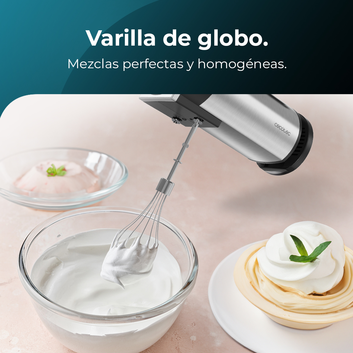 Una batidora de mano mezclando crema en un bol de cristal. Nata montada y postres al fondo. El fondo es rosa.
