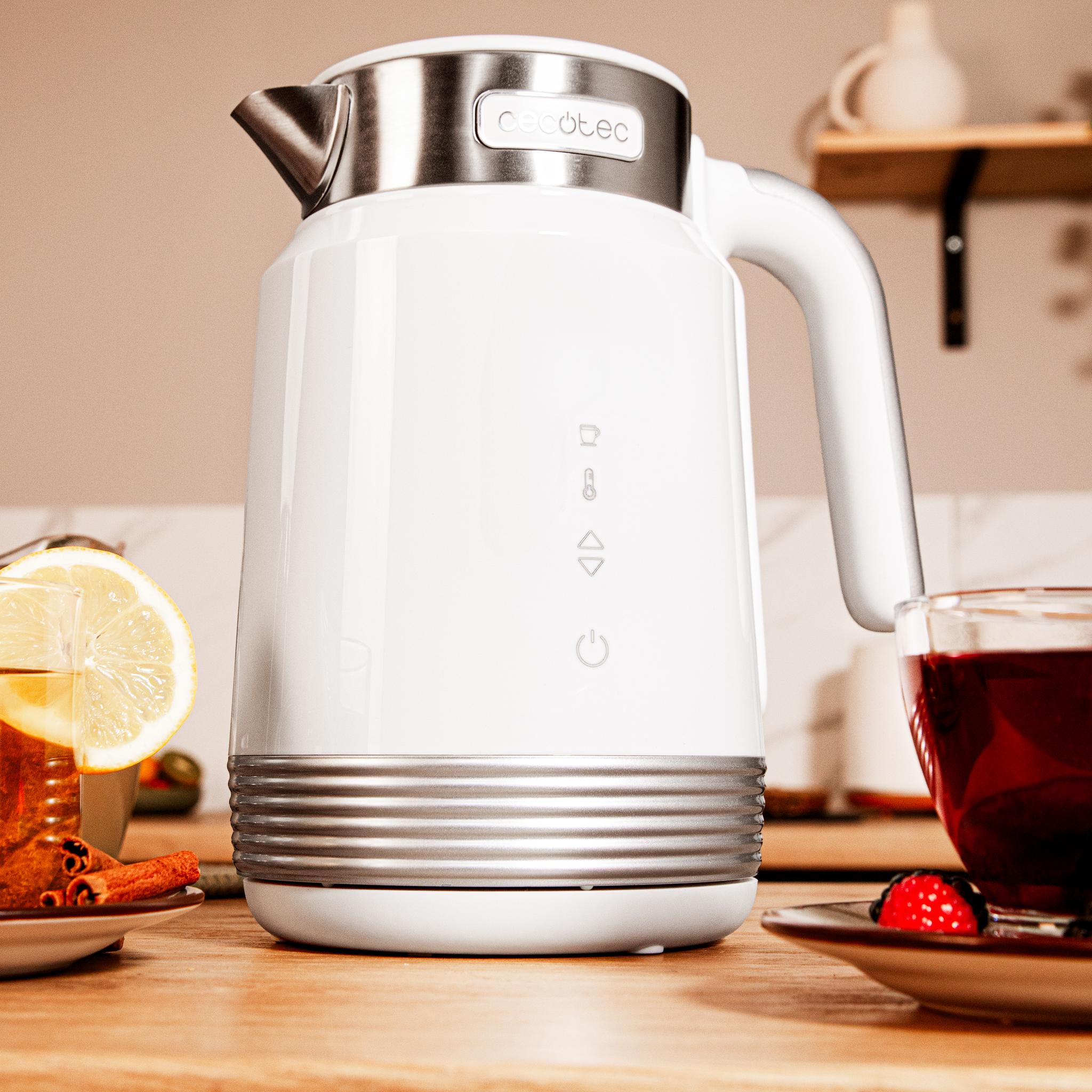 Hervidor eléctrico blanco, taza de té con limón, palitos de canela y una taza de té con una baya en un platillo.