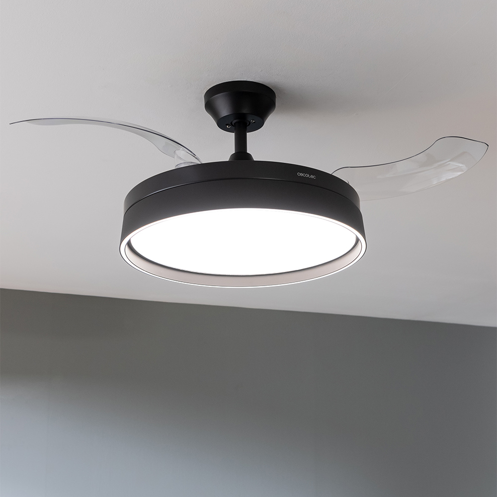 Un ventilador de techo negro con luz centrado. Las aspas son transparentes. El techo es blanco y la pared gris.