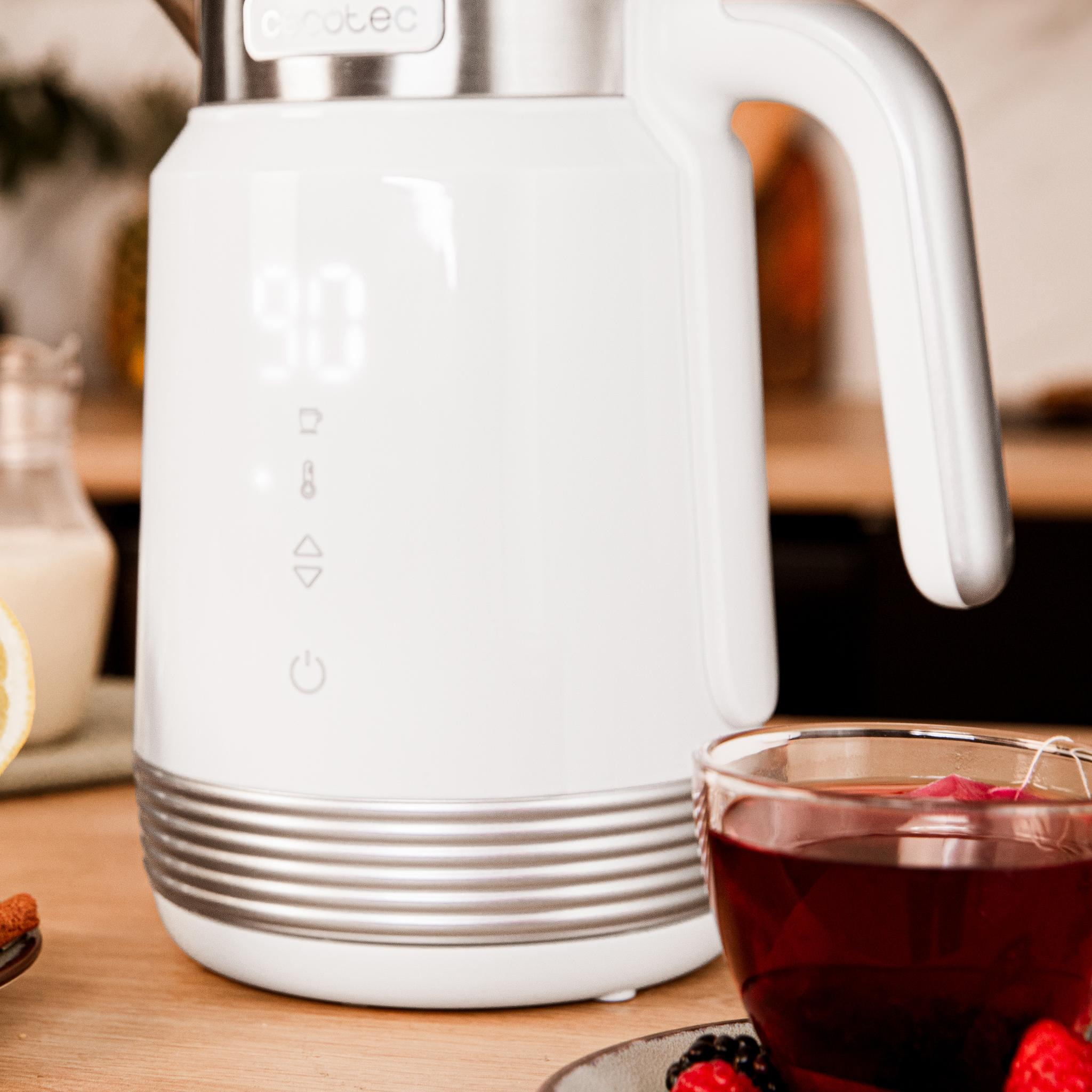 Una tetera eléctrica blanca muestra 90 grados. Una taza de té con bayas está en primer plano, con una jarra de leche.