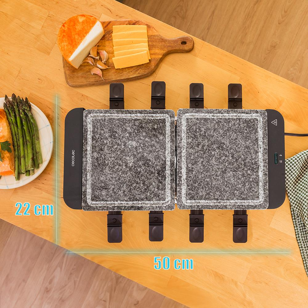 Una parrilla para raclette con queso, espárragos y ajo sobre una mesa de madera. Las dimensiones son 22 cm x 50 cm.