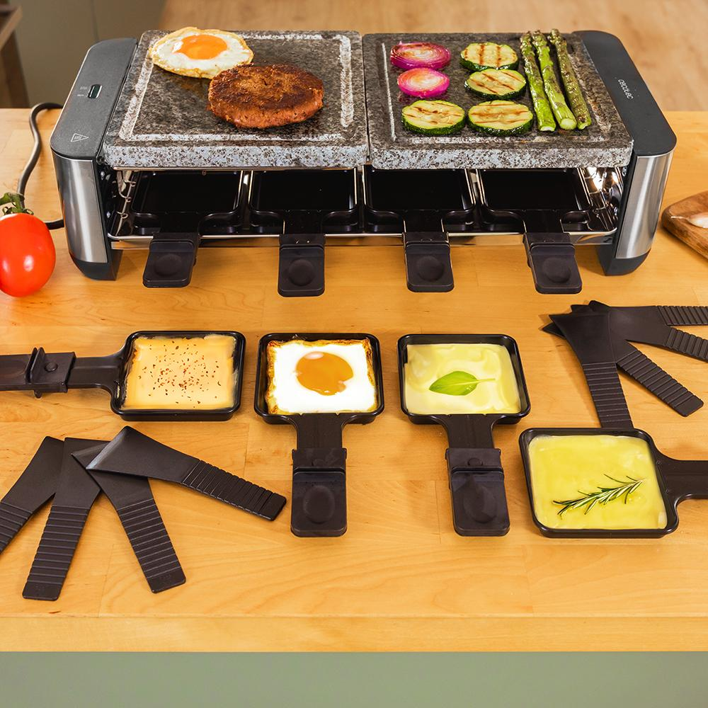Parrilla raclette con comida: huevo, hamburguesa, verduras y queso. Accesorios y tomate sobre mesa de madera.