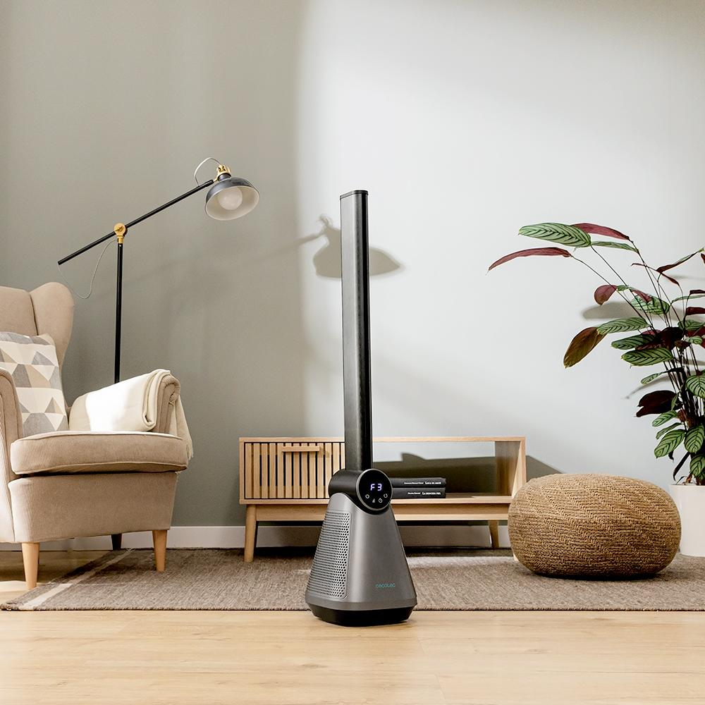 Salón con ventilador, sillón, lámpara de pie, mueble de madera, puf tejido y una planta.