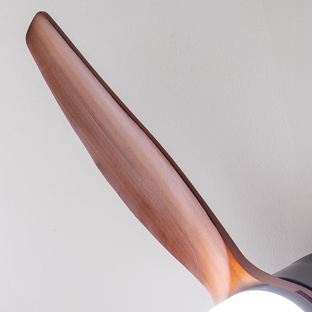 Primer plano de una aspa de ventilador de techo de madera sobre un fondo blanco. La hoja tiene un acabado de vetas de madera marrón. Una luz es visible.
