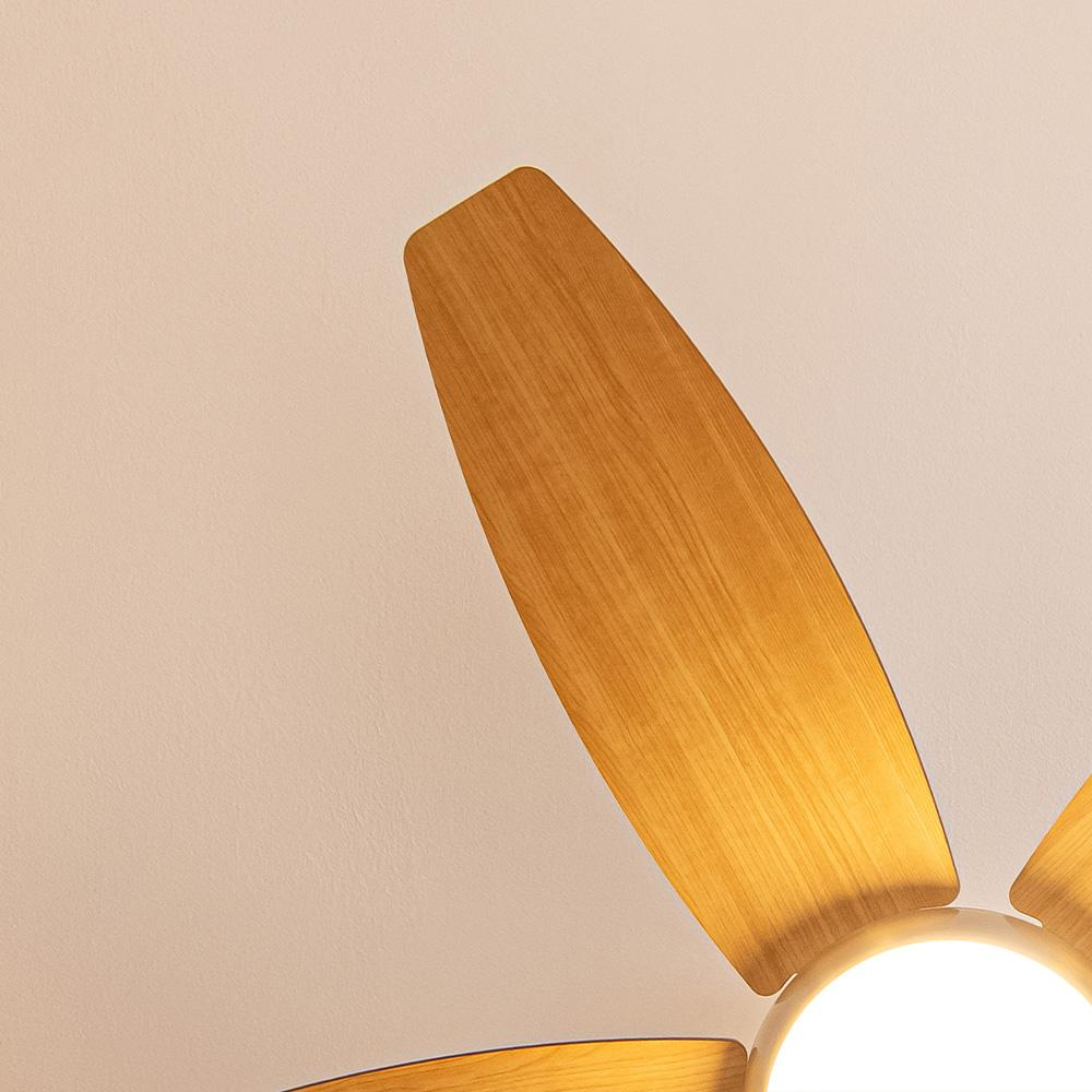 Primer plano de un ventilador de techo con aspas de madera contra un techo blanco. La luz del ventilador es visible.