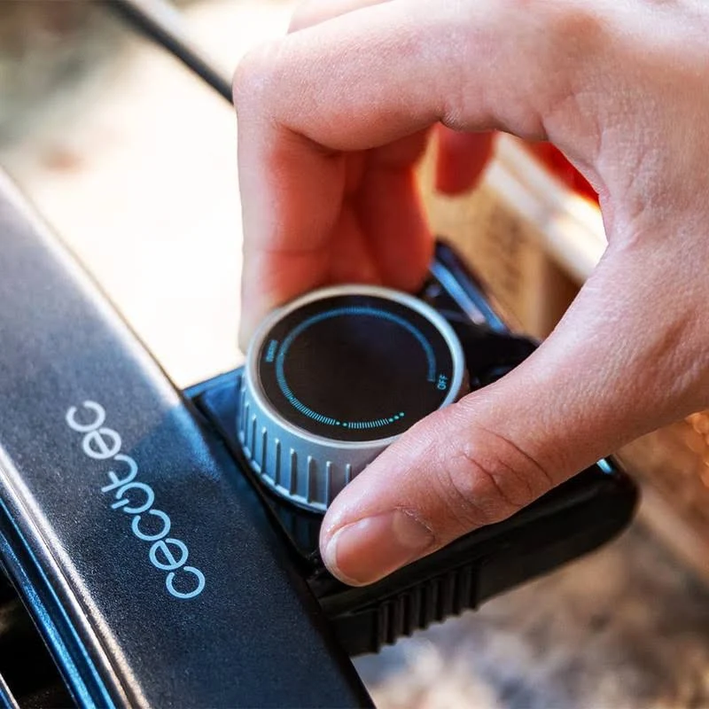 Una mano gira un dial en un electrodoméstico negro con la etiqueta 'Cecotec'. El dial es plateado y negro con indicadores azules.