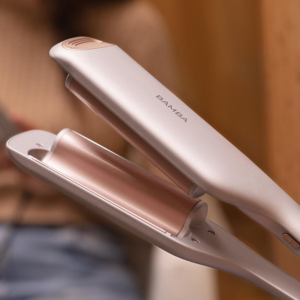 Primer plano de una plancha de pelo Bamba, oro rosa y plata, ligeramente abierta. El nombre de la marca es visible.