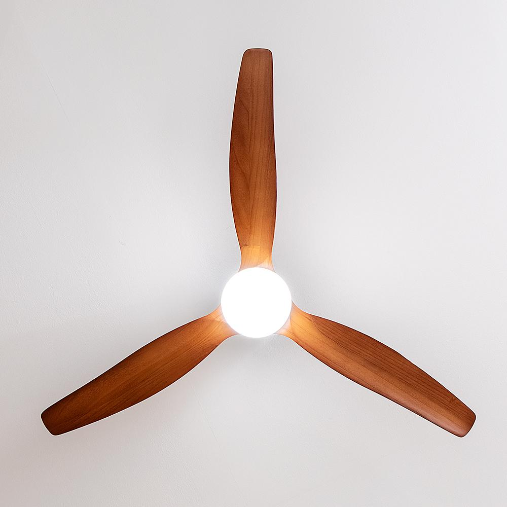 Un ventilador de techo con tres aspas de madera y una luz central sobre fondo blanco.