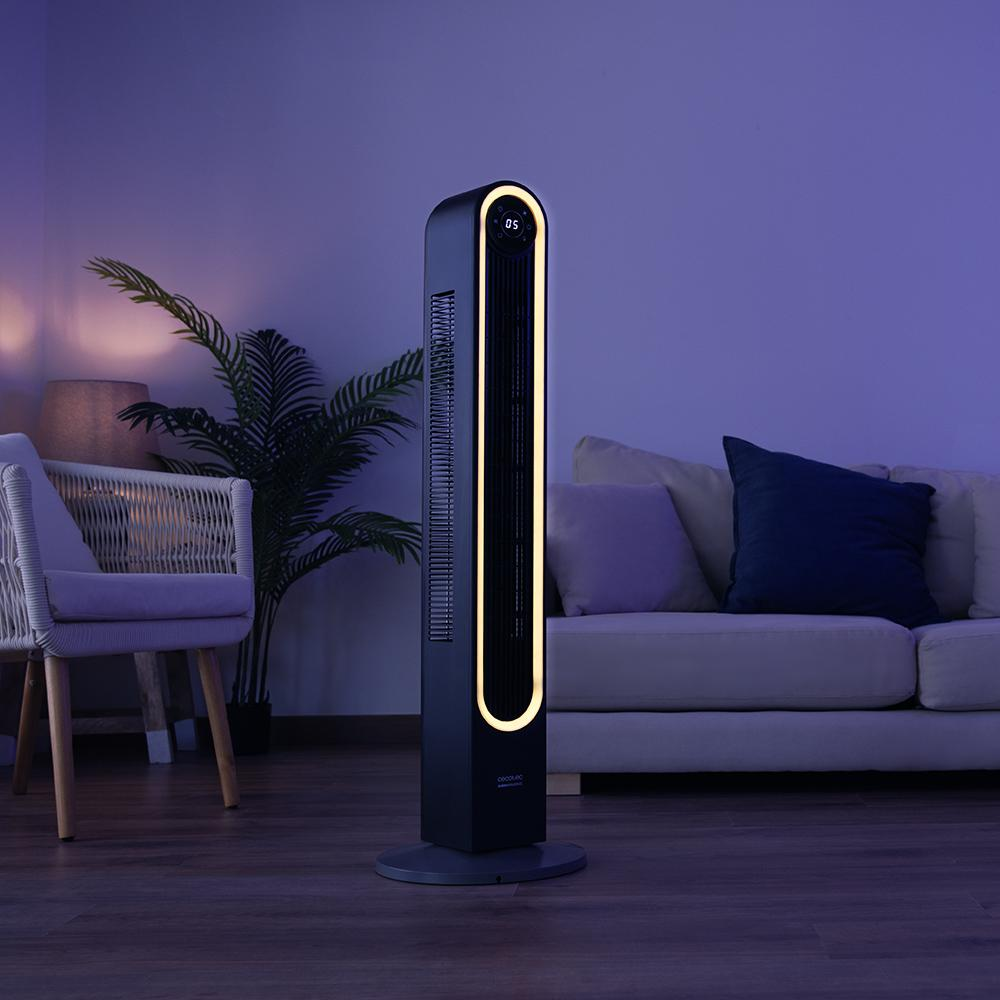 Un ventilador de torre negro con una tira de luz está en una habitación. También se ven una silla, un sofá y una planta.