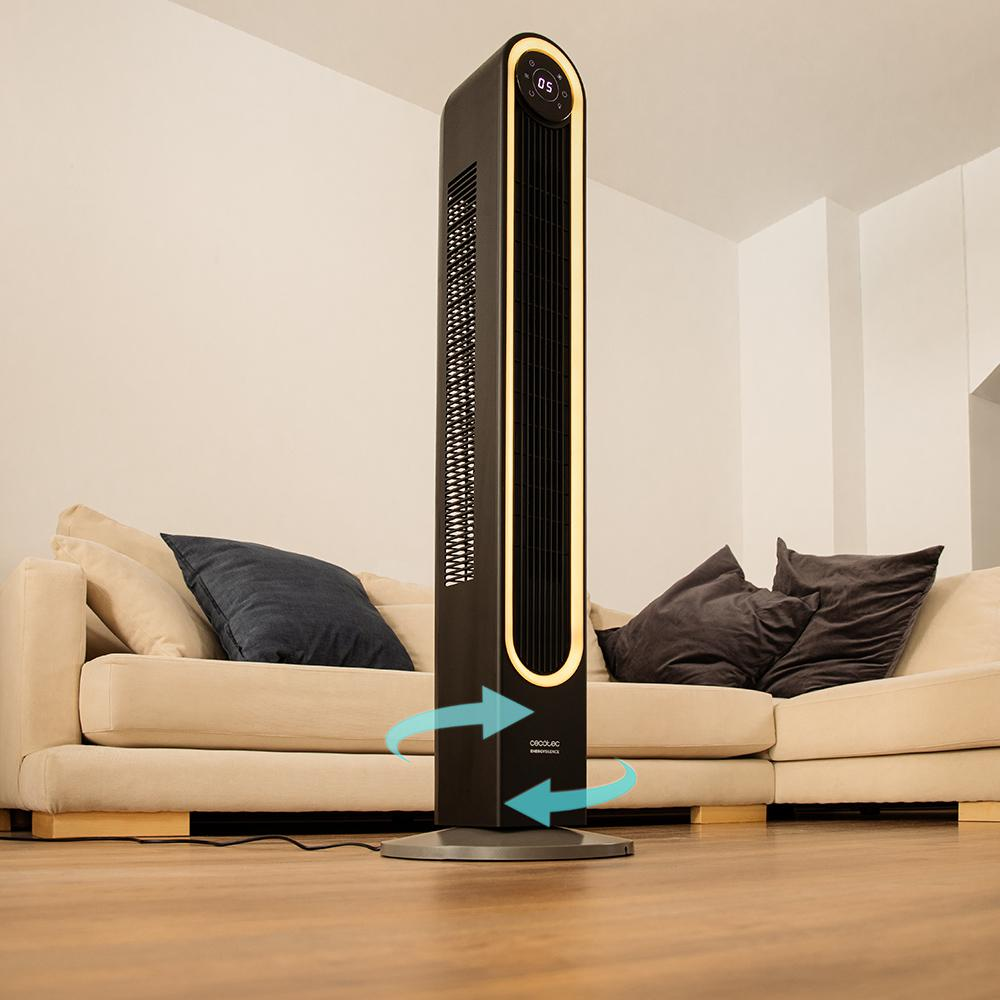 Un ventilador de torre negro en una sala de estar. Sofá beige y almohadas en el fondo. Suelo de madera.
