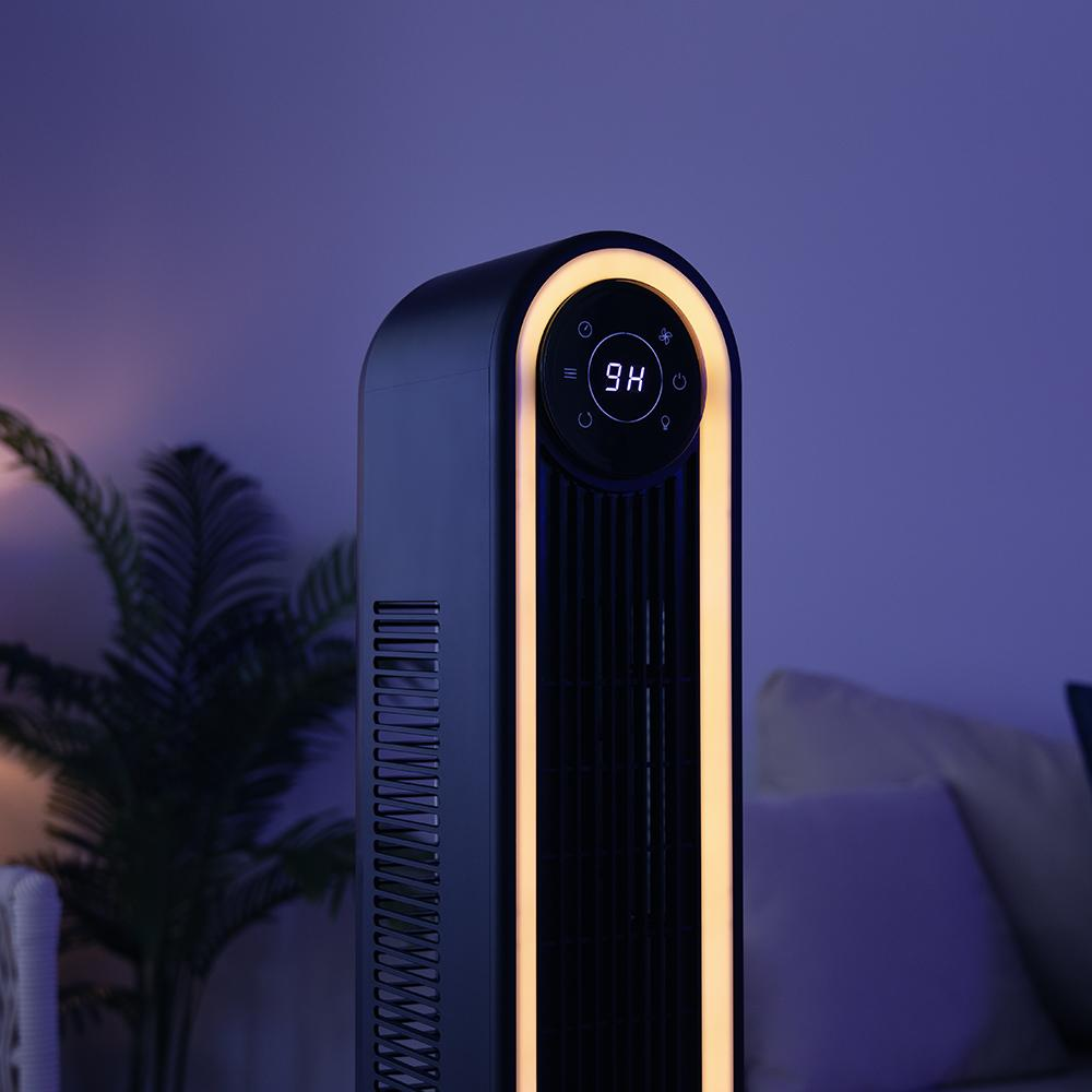 Un ventilador de torre negro con pantalla digital '9H'. Tiene una tira de luz amarilla y está frente a una planta.