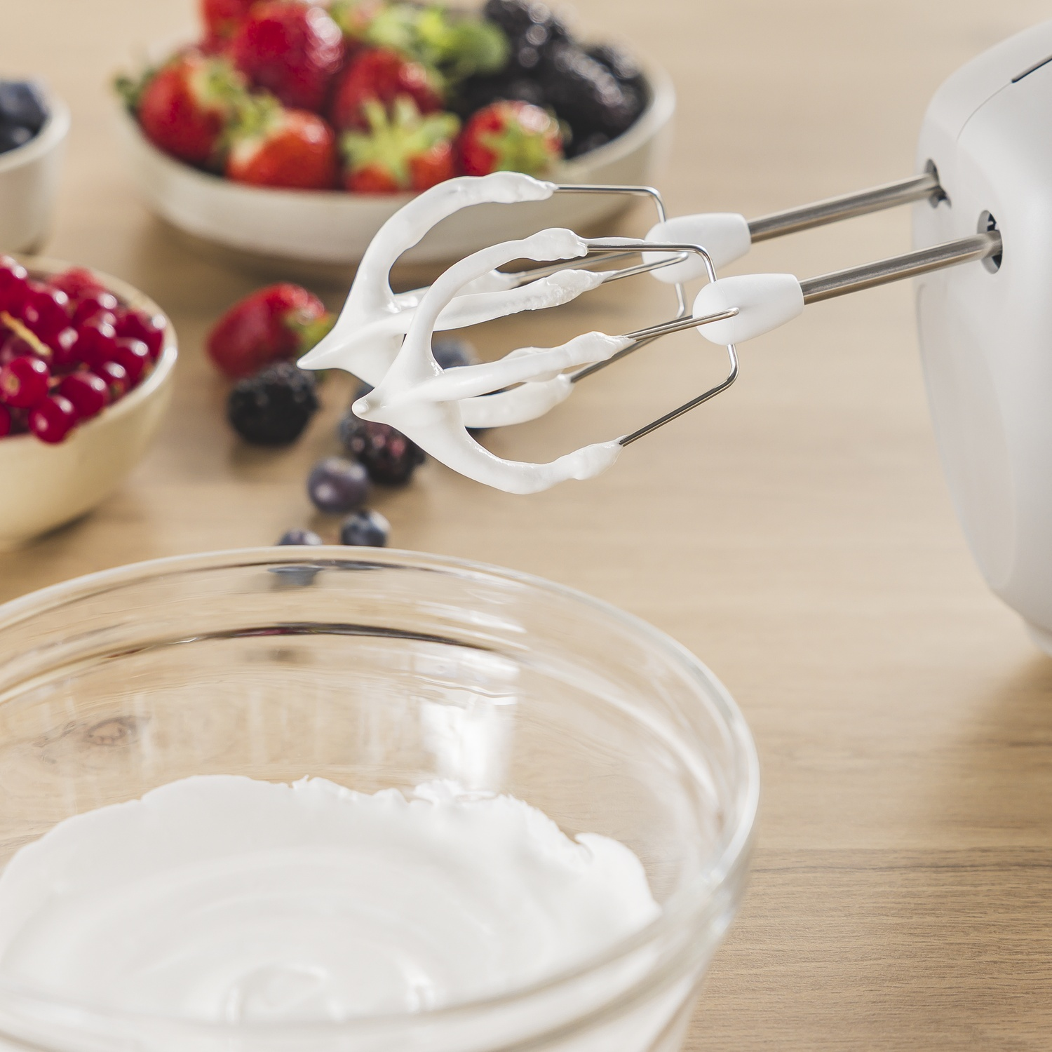 Een mixer klopt room voor bessen. Witte room zit in een glazen kom. Bessen zoals aardbeien en bosbessen zitten in kommen.