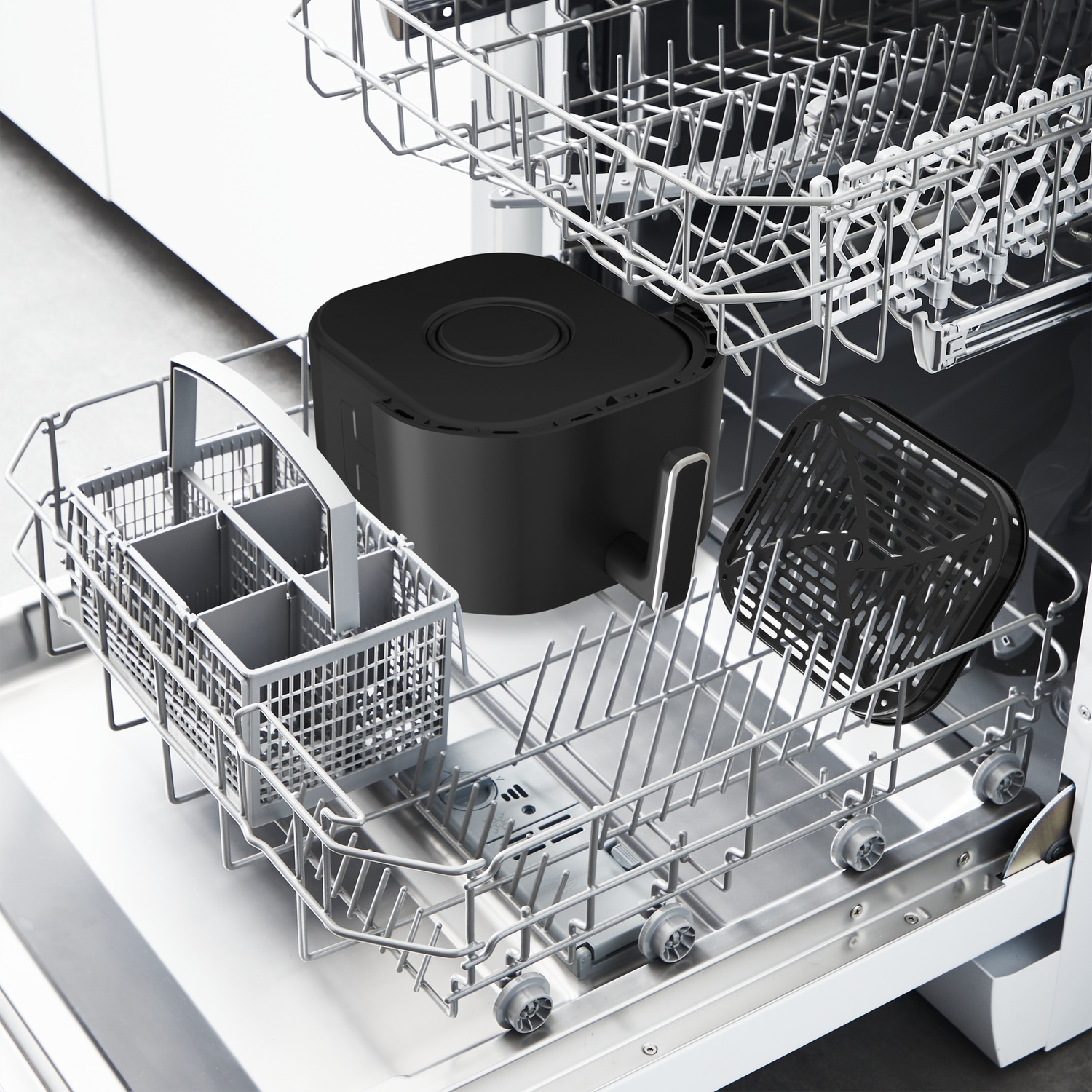 A black air fryer and its basket sit in a dishwasher. A silverware basket is in the lower left.