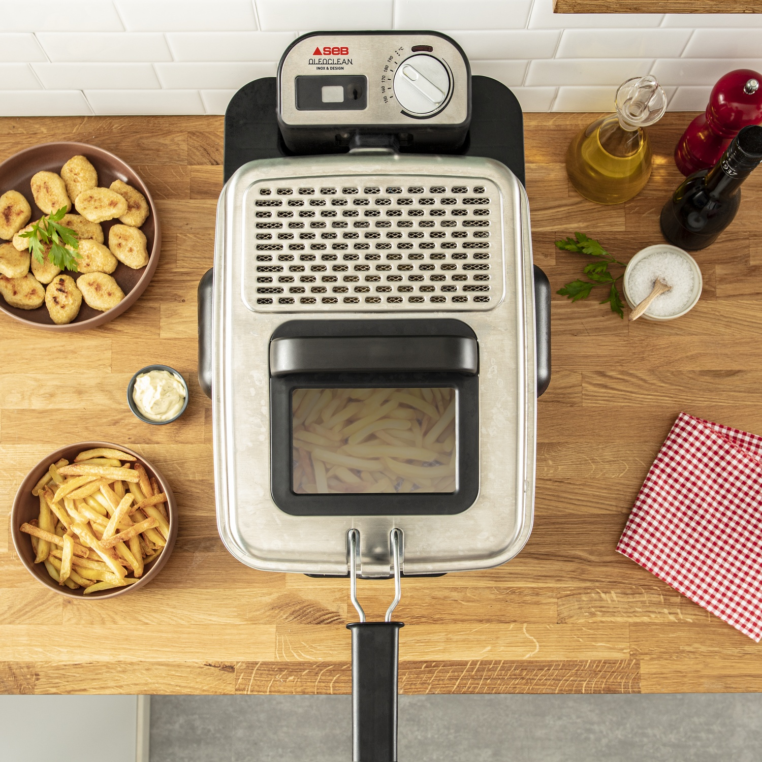 Une friteuse avec des frites et des nuggets sur une surface en bois. Huile, sel et poivrières sont également présents.
