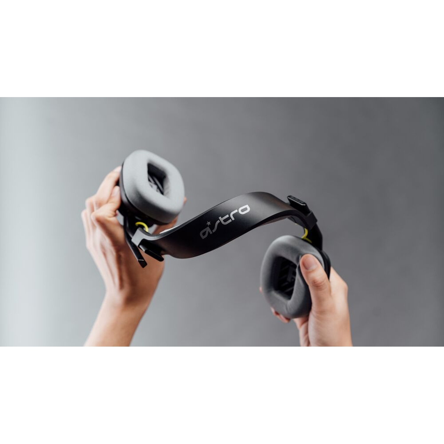 Mani che tengono un'auricolare da gioco Astro nera con padiglioni grigi su sfondo grigio. Il logo Astro è visibile sulla fascia.
