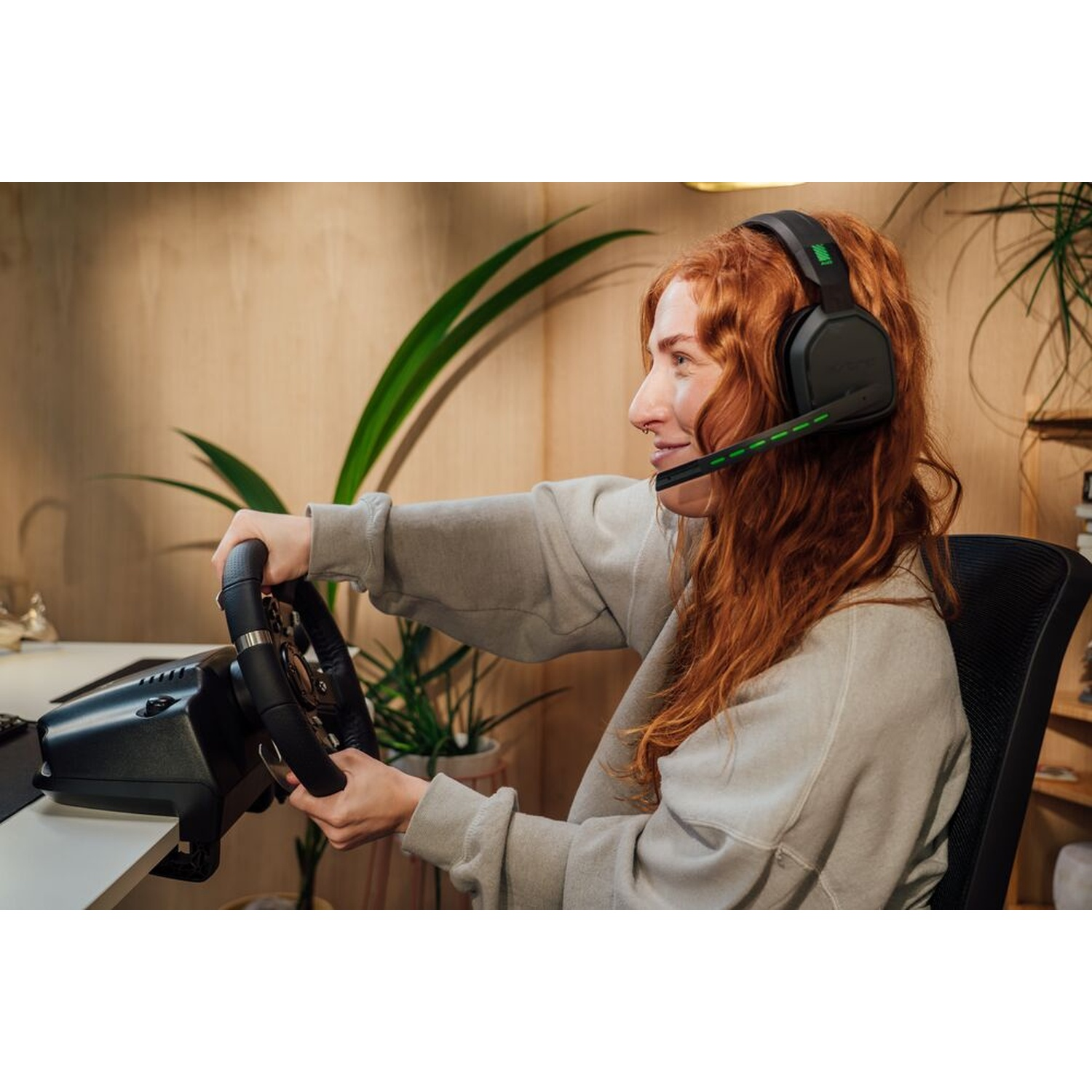 Una donna dai capelli rossi con le cuffie tiene un volante. È davanti a un muro di legno, sta giocando.
