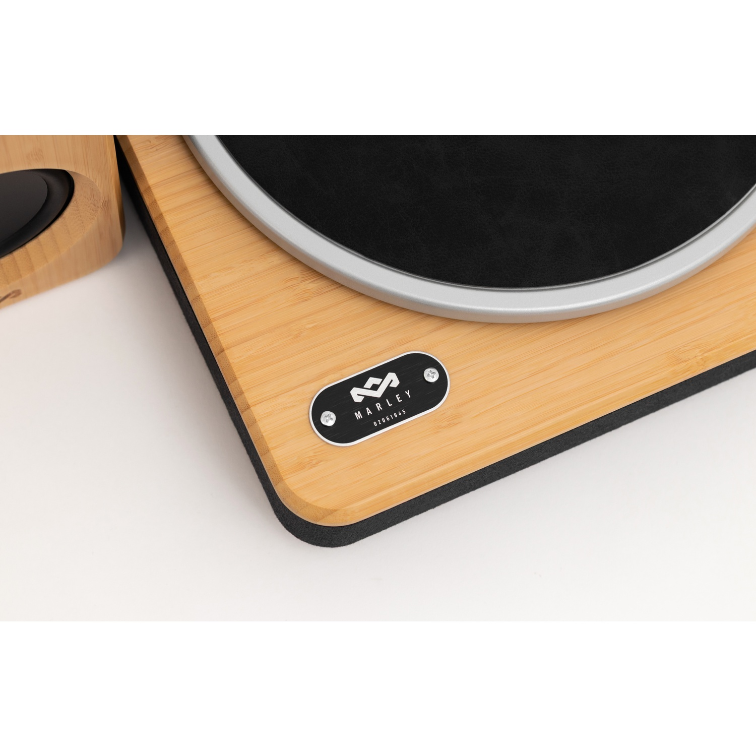 Une platine vinyle en bois avec un disque noir. Le bord argenté entoure le disque. Un haut-parleur est à gauche. Le logo Marley est visible.