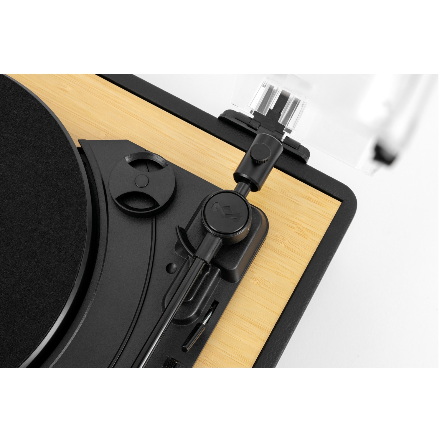 Close-up of a turntable. Black components on light wood. A black record is visible. Clear plastic cover and tone arm.