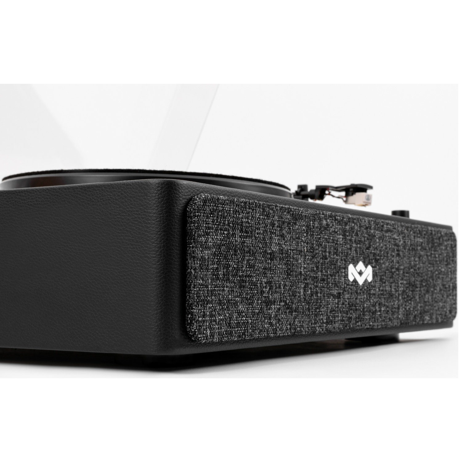 A close-up of a black record player. It has a fabric speaker cover and a silver logo. The background is white.